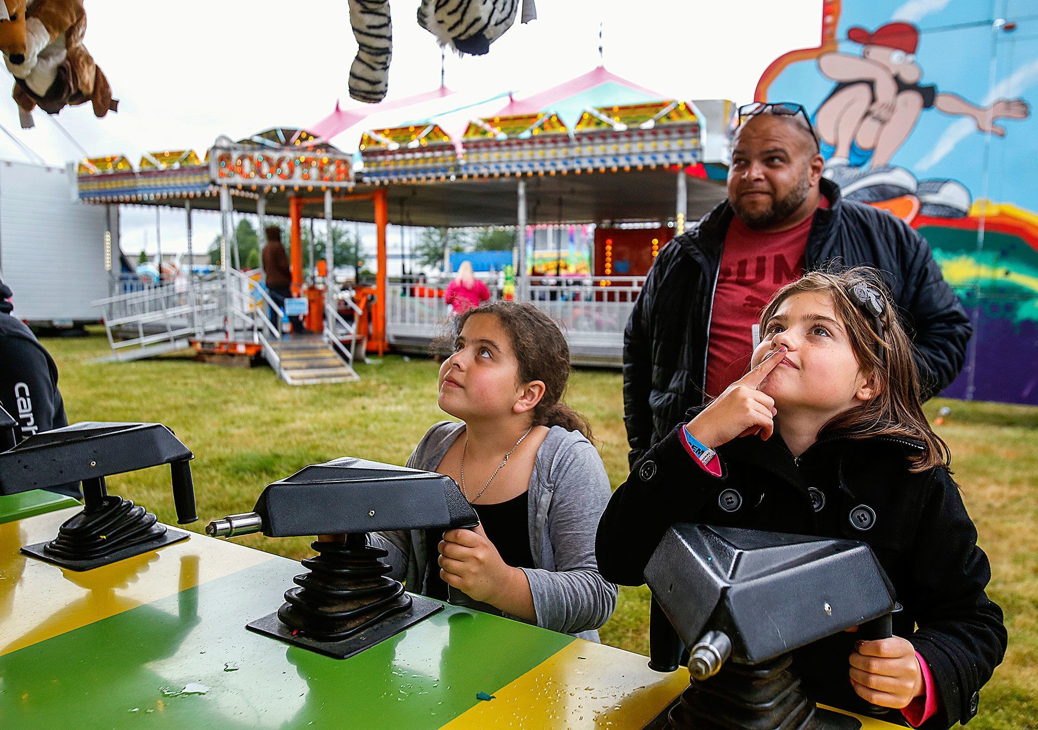 Lily Hobbs, 9, (right) of Arlington, contemplates which prize stuffed animal to take home with her after winning in the Carnival’s water gun gallery, Thursday night. Ready for game 2, Adriana Rodriguez, also 9 (middle), eyes the prizes, too! (Dan Bates / The Herald)