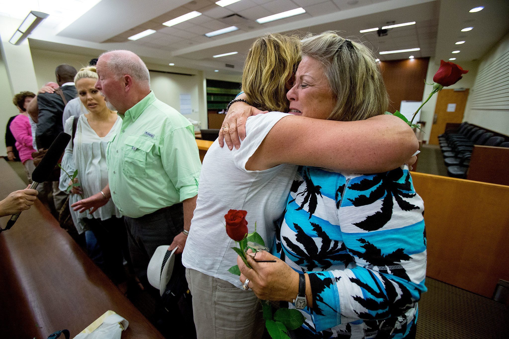 Denise Webber, right, is hugged by Lori Burkheimer after a guilty verdict in the re-trial of John Alan Whitaker, for the murder of Webber’s daughter, Rachel Burkheimer, at the Snohomish County Courthouse on Thursday in Everett. At left, Rachel’s father, Bill Burkheimer, talks to the media as her sister, Meaghan Burkheimer-Hoang, listens in. (Andy Bronson / The Herald)