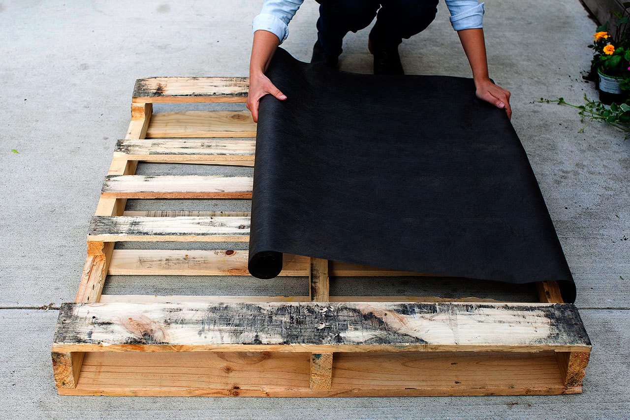 Lay your pallet flat, with the side you want facing front on the ground; it should have several horizontal planks. Start measuring landscaping fabric across pallet. (Photo by Amy King, The Washington Post)