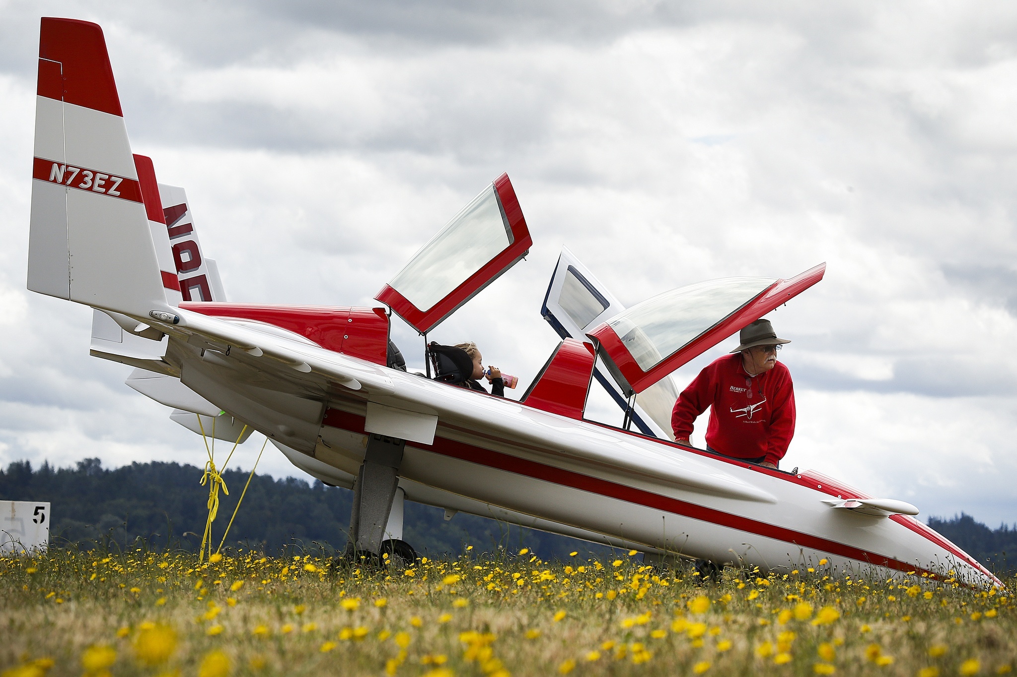 David Orr (right) stands next to his Berkut 360 airplane as his granddaughter Taylor Orr, 5, takes a sip of her juice from the rear seat at the Arlington Fly-In on Friday, July 8, 2016. “I like it,” Taylor said of flying with her grandfather, “I liked [seeing] the volcanoes.” The pair flew up from San Diego together on Thursday for the annual aviation event that features airshow performances, plane rides and camping on the grounds of the Arlington Municipal Airport. (Ian Terry / The Herald)