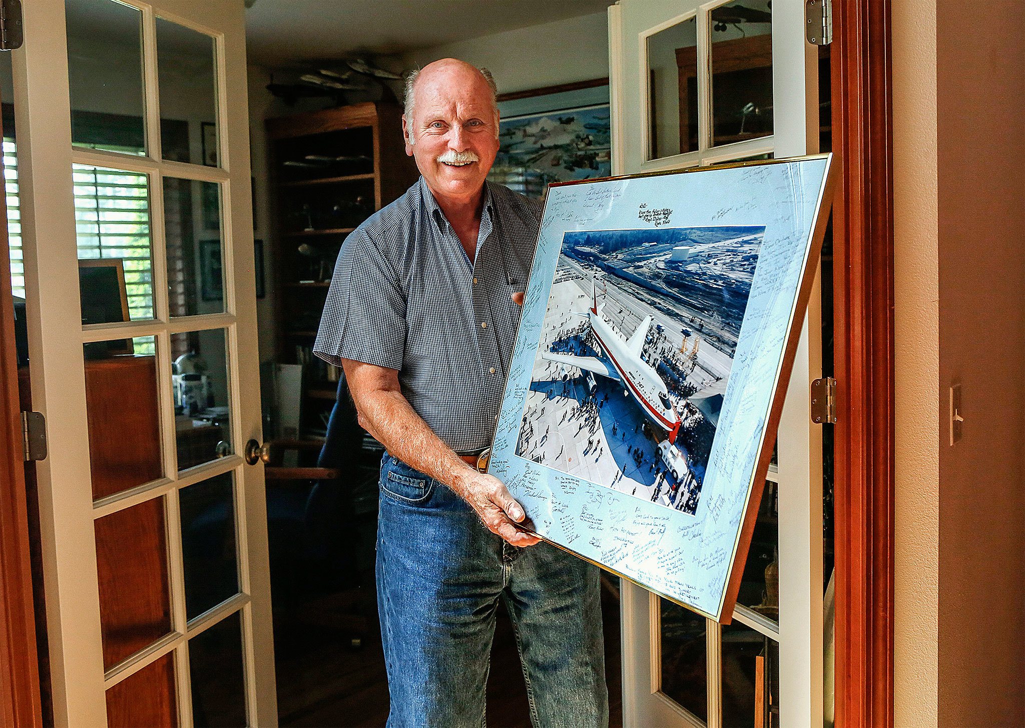 Bill Bruns hauls a matted and framed photo of the Boeing 787 rollout that was signed by his coworkers for him upon his retirement from Boeing. (Dan Bates/The Herald)