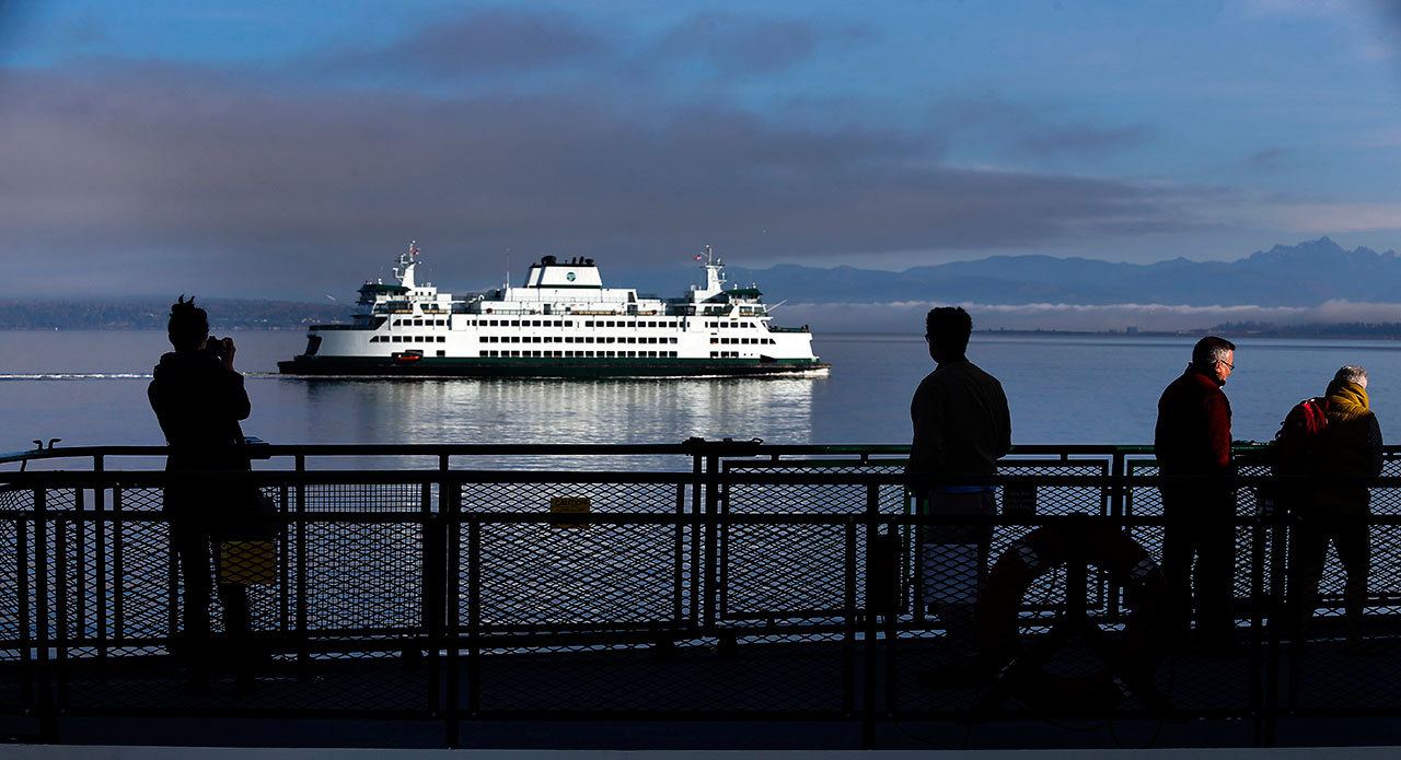 Passengers on the shady westbound end of the ferry from Mukilteo to Clinton, on Whidbey Island, watch and photograph the eastbound ferry during a crossing in April. (Dan Bates / Herald file)