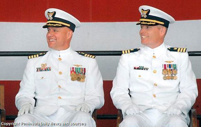 Capt. Andrew Eriks, outgoing commanding officer of U.S. Coast Guard Air Station/Sector Field Office Port Angeles, left, and Cmdr. Mark Hiigel listen to comments from the podium during a ceremony Friday to install Hiigel as the base’s new commanding officer. (Keith Thorpe/Peninsula Daily News)