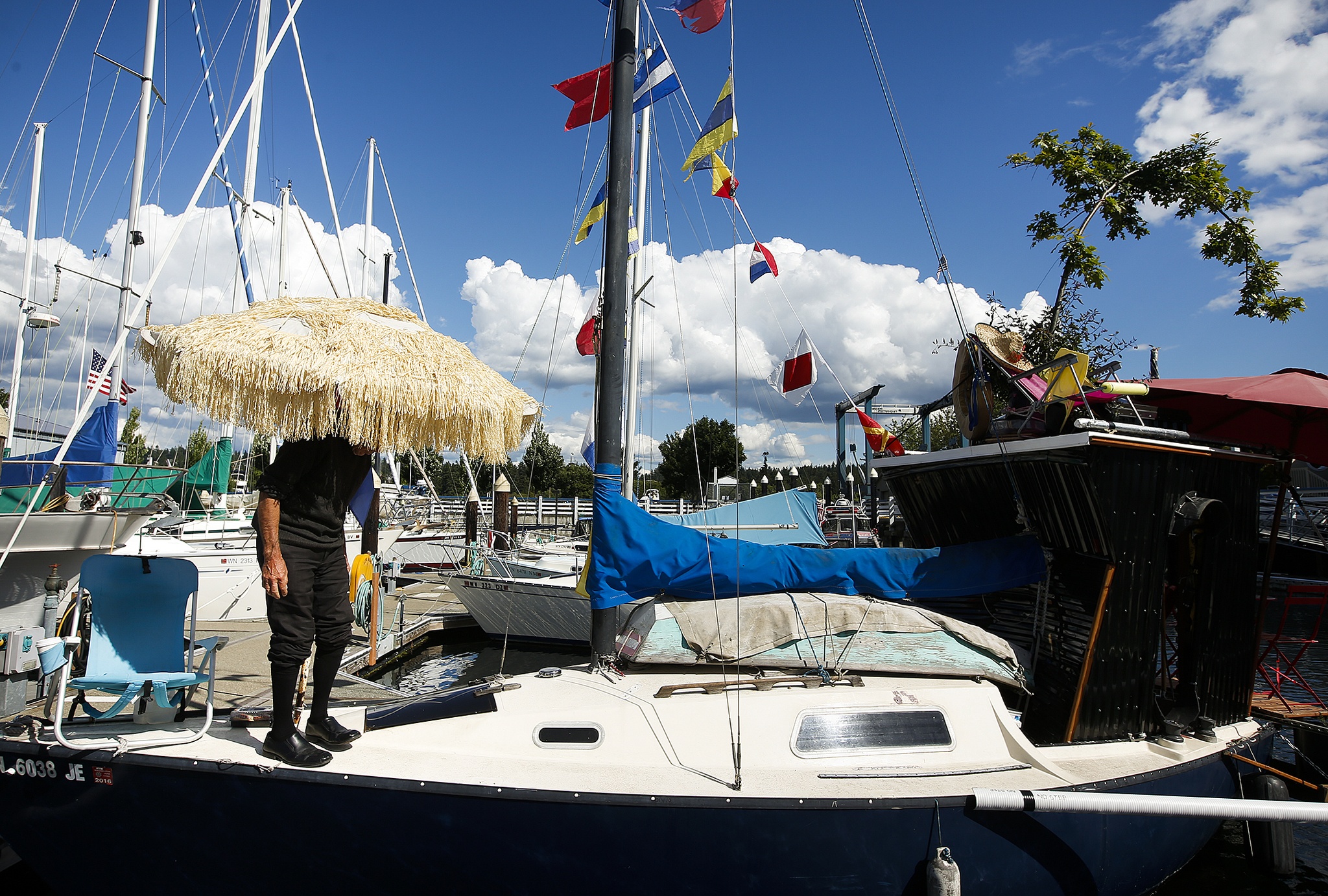 Ian Terry / The Herald                                William Anderson stands on his 24-foot sailboat moored at the Port of Edmonds near Anthony’s Homeport on Thursday, June 16, 2016. Anderson’s customizations include a tiki umbrella, a small room on the stern made from plastic siding, colorful flags and a pin oak tree he salvaged from a Home Depot for $10.                                Photo taken on 06162016