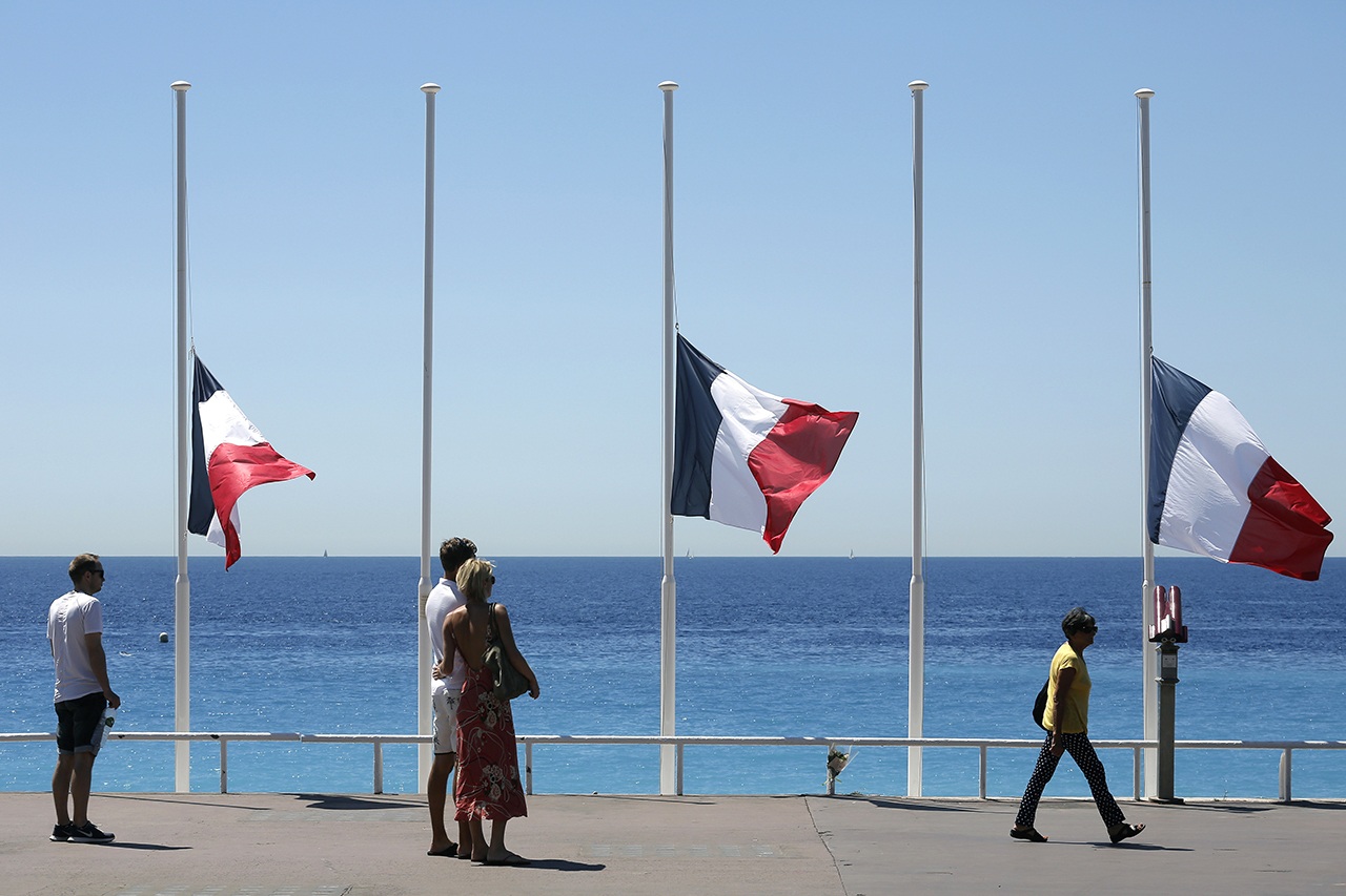 People stroll on the Promenade des Anglais with the French flag at half staff near the scene of a truck attack in Nice, southern France, on Saturday. (AP Photo/Laurent Cipriani)