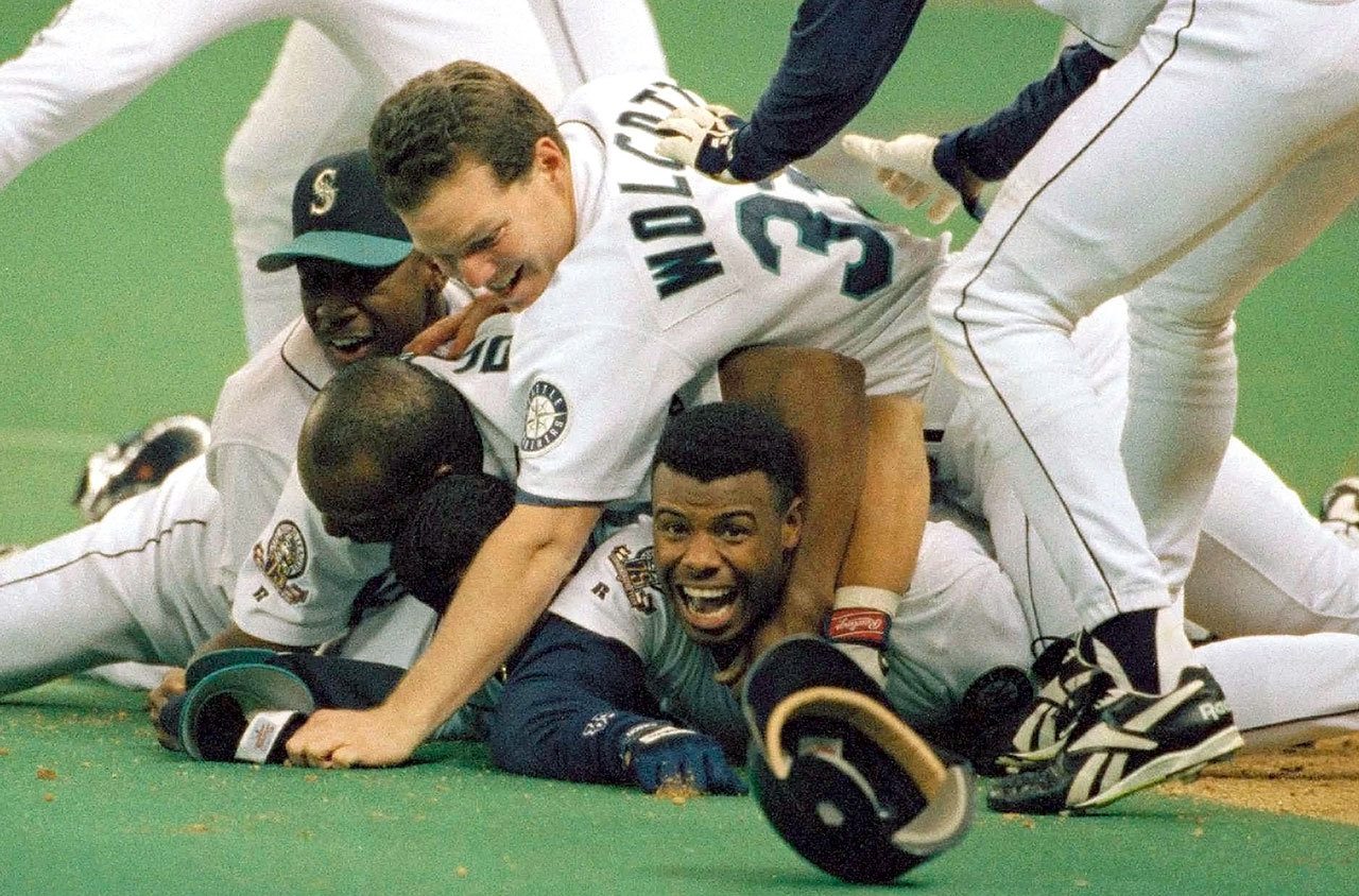 In this photo from Oct. 8, 1995, Seattle’s Ken Griffey Jr. smiles from underneath a pile of teammates who mobbed him after he scored the winning run in the bottom of the 11th inning of Game 5 of a best-of-five playoff series against the New York Yankees. (AP Photo/Elaine Thompson, File)