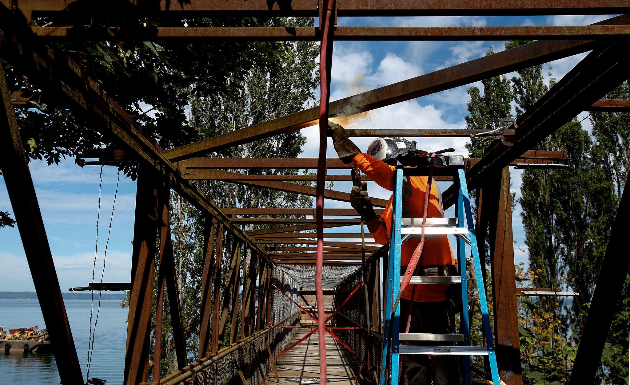 Corona Steel ironworker Abraham Rodriquez welds a brace in place on the pedestrian bridge at Howarth Park in Everett on Monday. The bridge and beach access have been closed since May 2015, when an inspection uncovered deterioration on the bridge’s steel beams that support its walking surface. Repairs to the bridge are expected to be finished in September. (Andy Bronson / The Herald )
