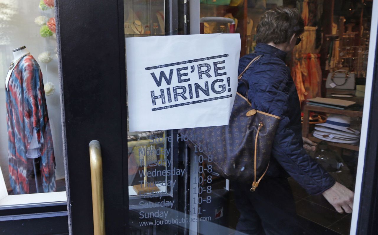 A woman passes a “We’re Hiring!” sign while entering a clothing store in the Downtown Crossing of Boston on May 18.