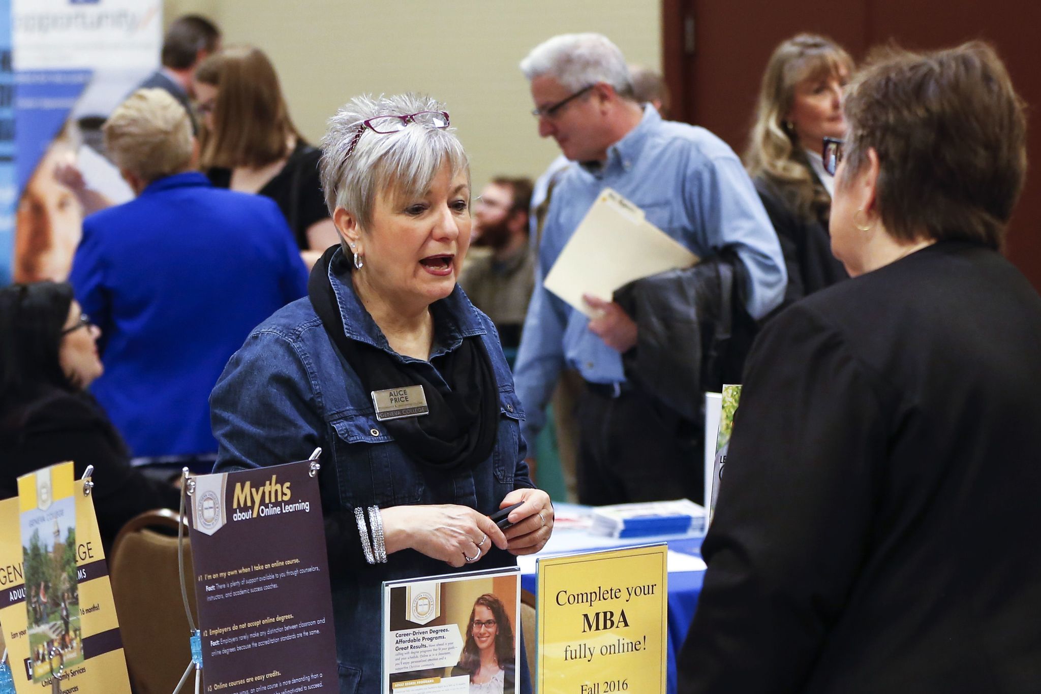 In this March 30 photo, Alice Price, educational outreach specialist for adult and graduate studies at Geneva College, speaks with a visitor to her table at a job fair in Pittsburgh.