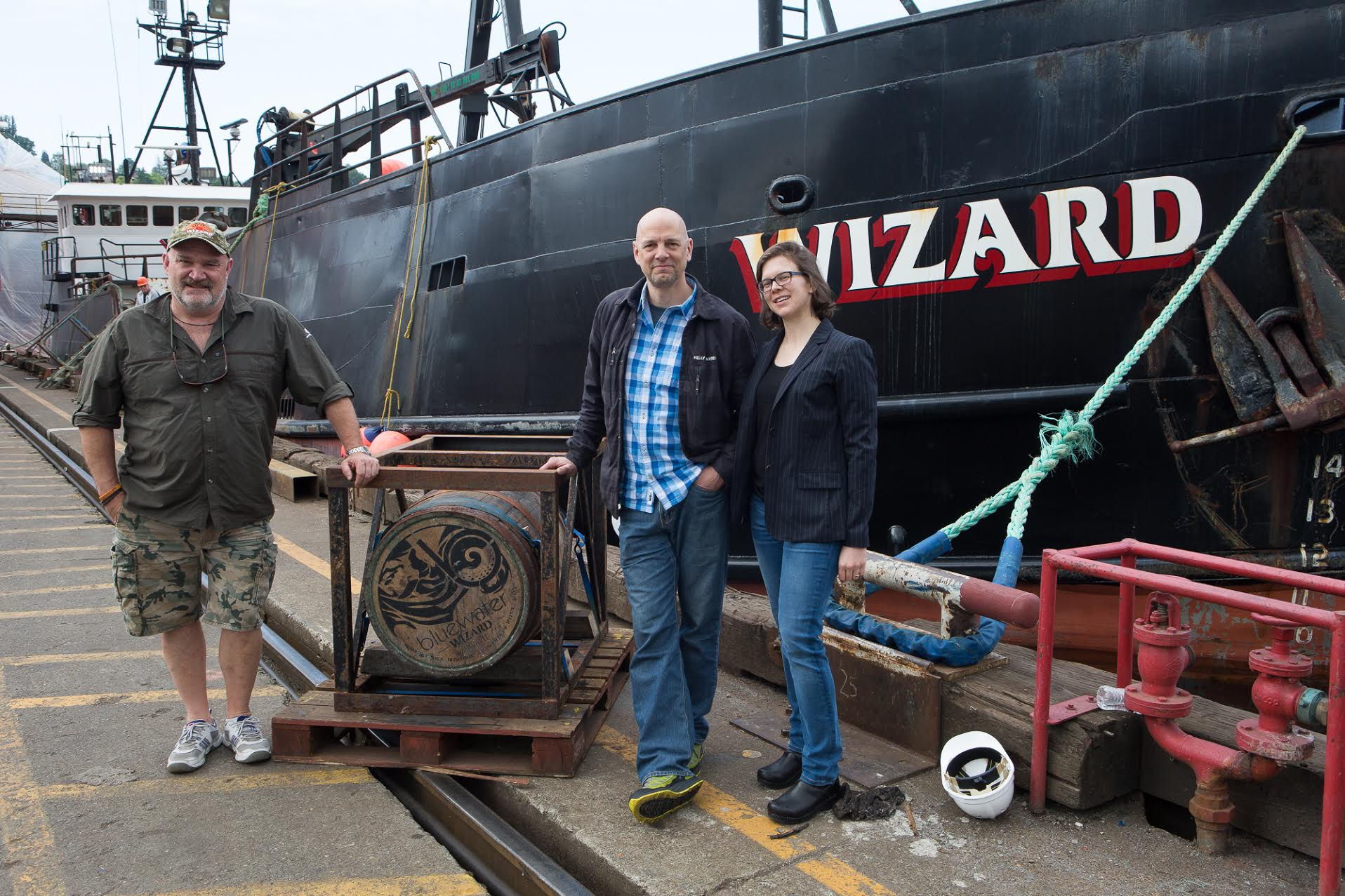 Capt. Keith Colburn (left) stands Bluewater Organic Distilling owner John Lundin and his wife, Jessica, beside the barrel of akvavit that rode on the F/V Wizard during the crabbing season in the Bering Sea.