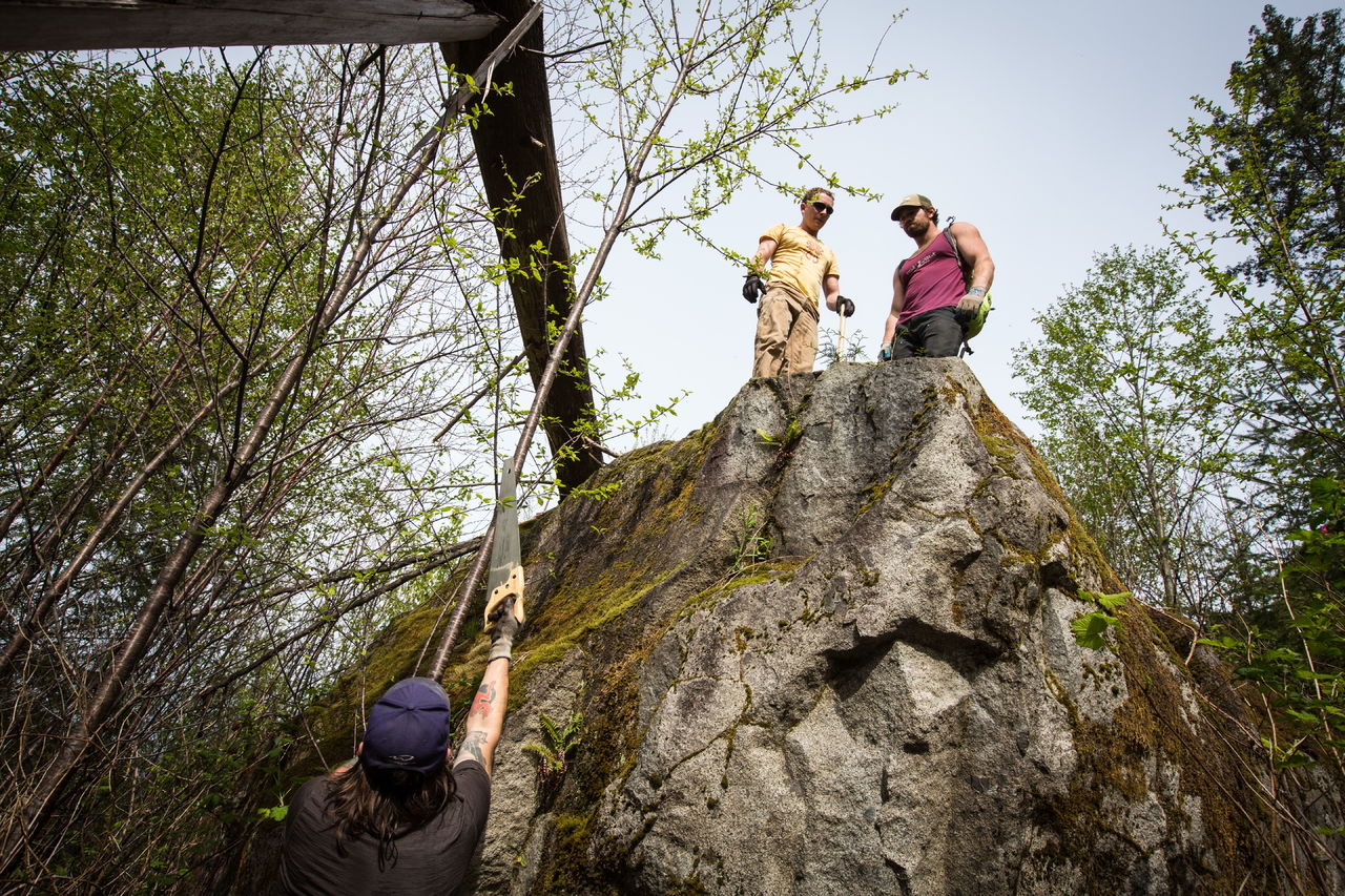 Kelly Sheridan and Miles Berkey watch as Bela Stoll saws a tree off a boulder while working to clear trails April 16 near Gold Bar.