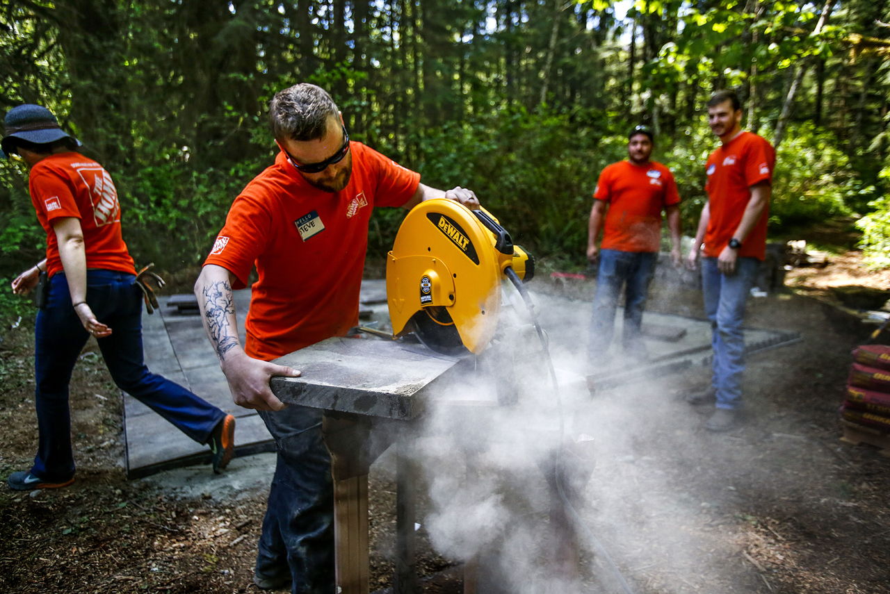 Home Depot volunteers, Christopher Sweeney (far right) and Tony Cozadd stand back while Stephen Grabowski uses a masonry dry saw to cut a heavy slab for the talking circle at Healing Hearts in Hope Veteran’s Retreat Center on Teresa “Flying Eagle” Baird’s property outside of Granite Falls.