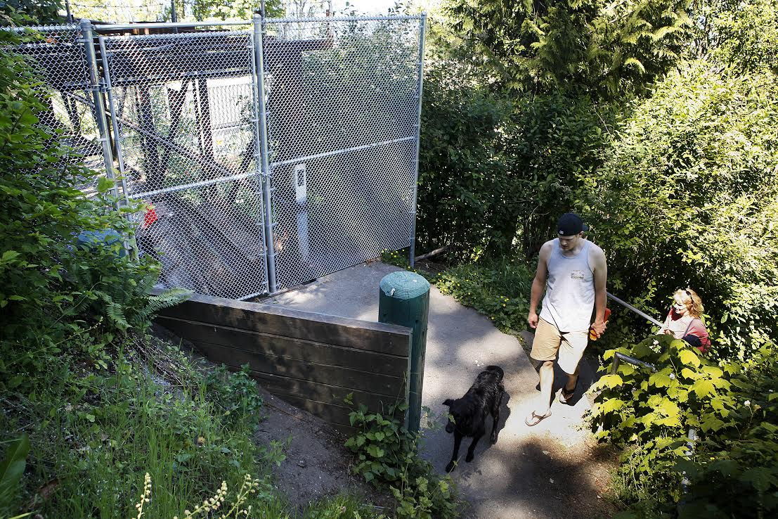 Mark Schireman, of Everett, walks past the closed entrance to the footbridge leading to Howarth Park‘s beach in Everett on Tuesday with his mother, Mary Schireman, and their dog, Ryelee, a flat-coated retriever. “What makes me sad is I know there are a lot of high school kids crossing the tracks,“ Mary said. “It‘s really our only beach access around here.”