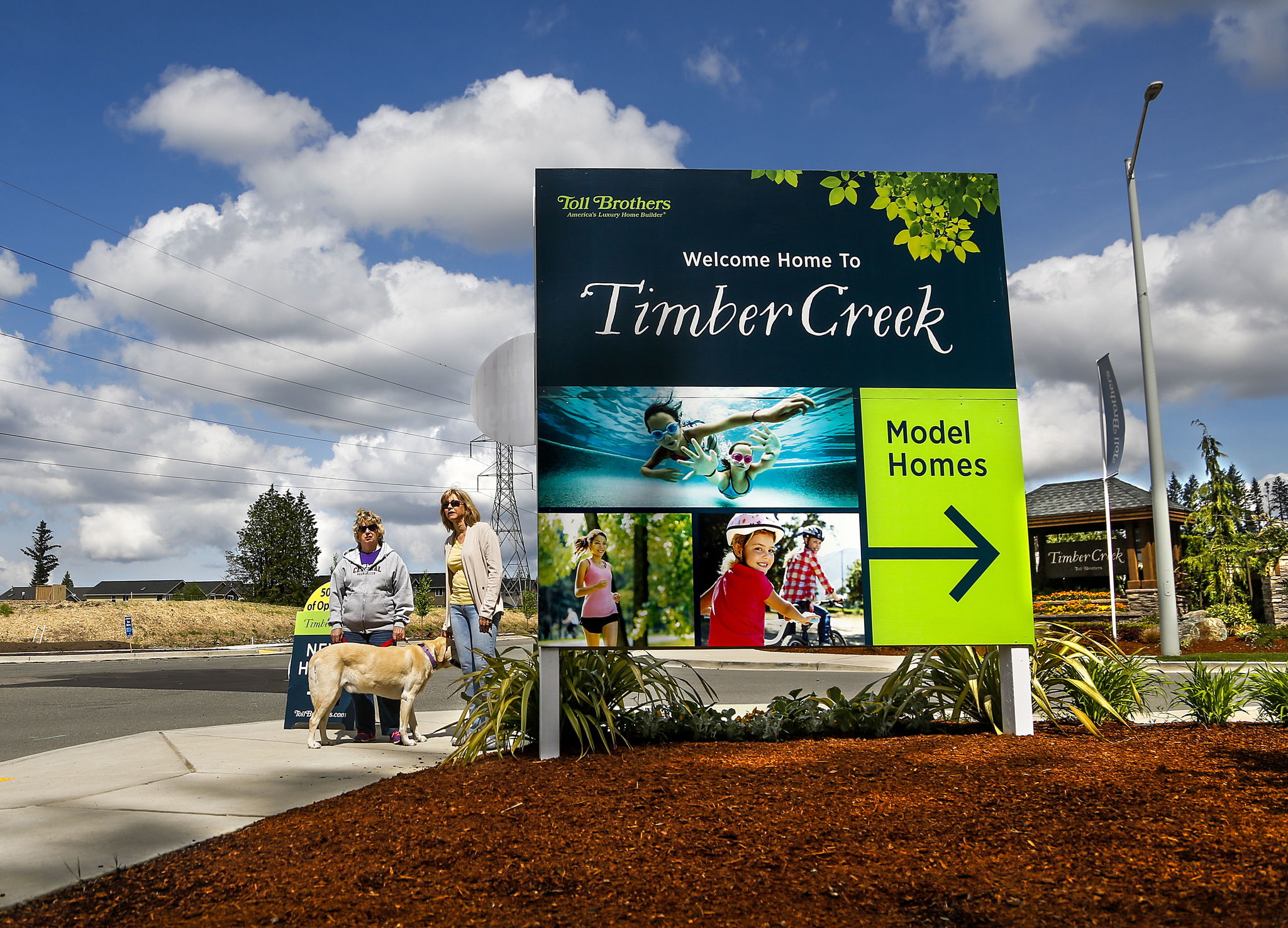 Neighbors, Caroline Atwood, left, with her dog, Buddy, and Leslie Foley look toward their own homes down 43rd Ave SE, from the entry to Timber Creek development. Their own peaceful country life has deteriorated over the last three years, Atwood says. The dump trucks alone are a game changer.