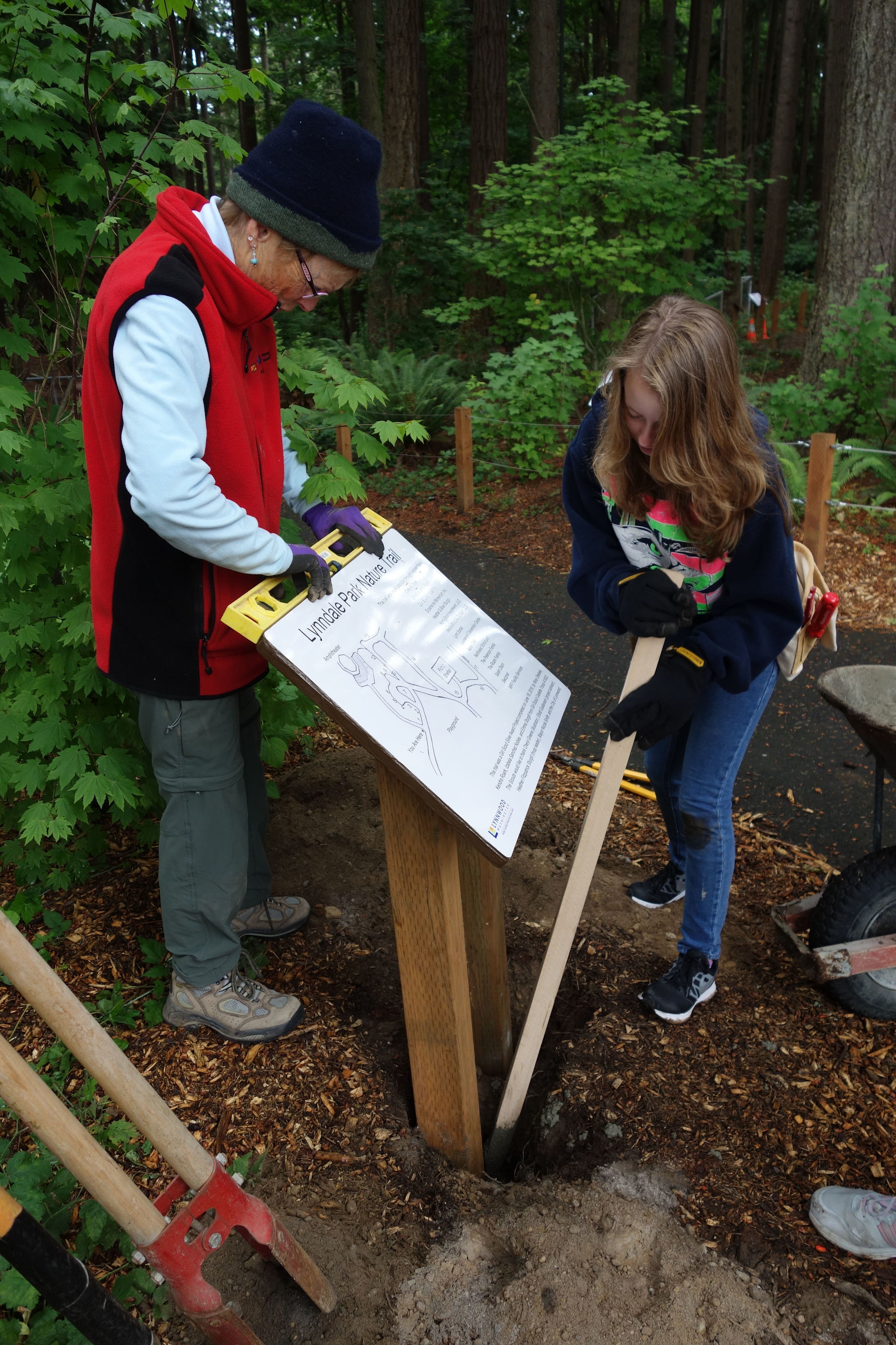 Lake Forest Park artist Cheryl Greene helps Girl Scout Kendra Roark (right) with the installation of one of the signs on a new interpretive trail at Lynndale Park in Lynnwood. Greene did the illustrations for the signs.