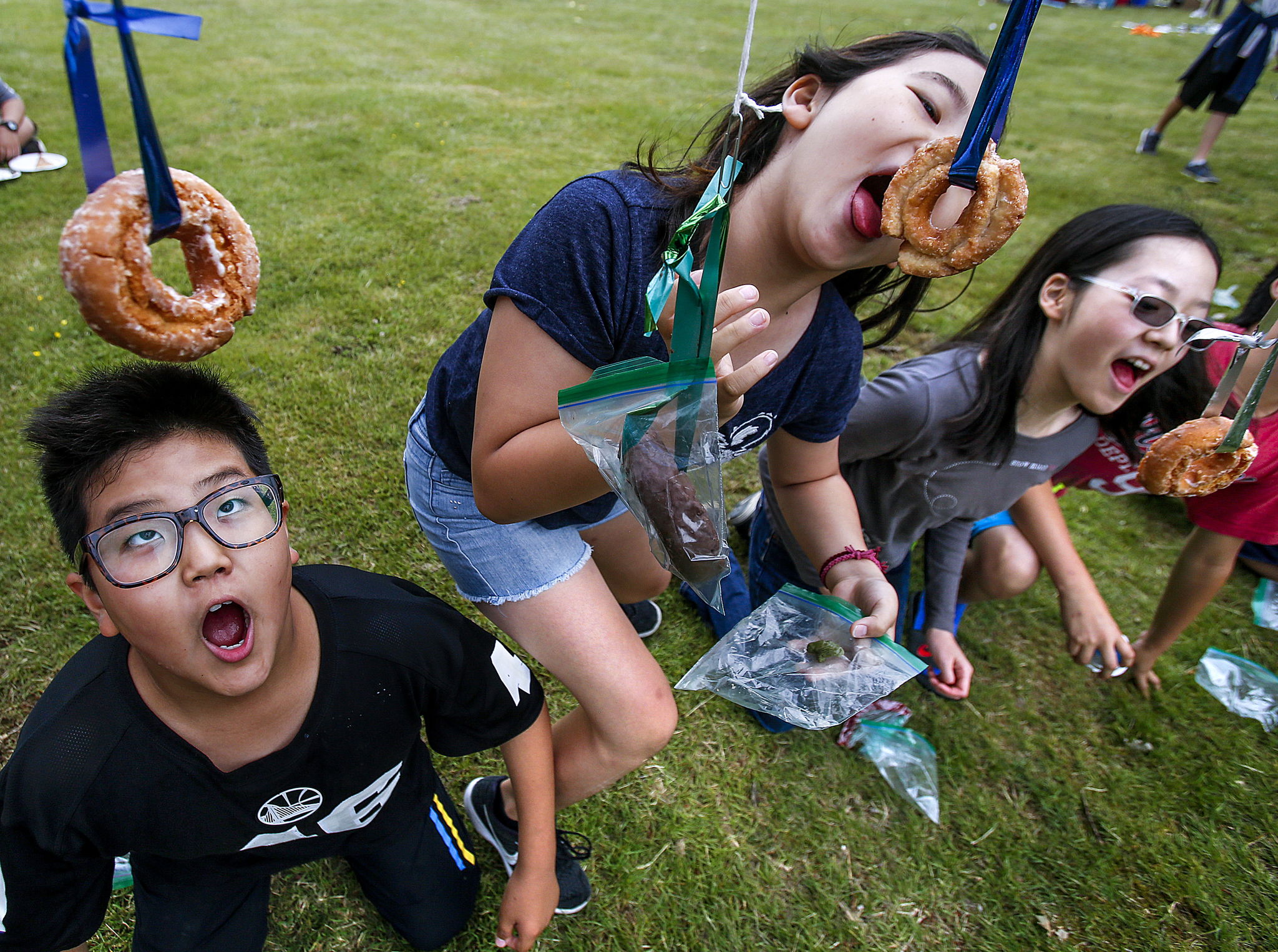 After removing the plastic bags, 12-year-olds Ocean Jang (left), Treety Jang and Sheamin Kim go after doughnuts on a string without using their hands Monday while competing in The Hungry Games outside Arlington Library.