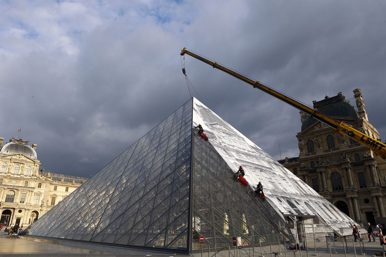 Technicians paste a giant picture on the glass Louvre Pyramid in Paris on Monday.