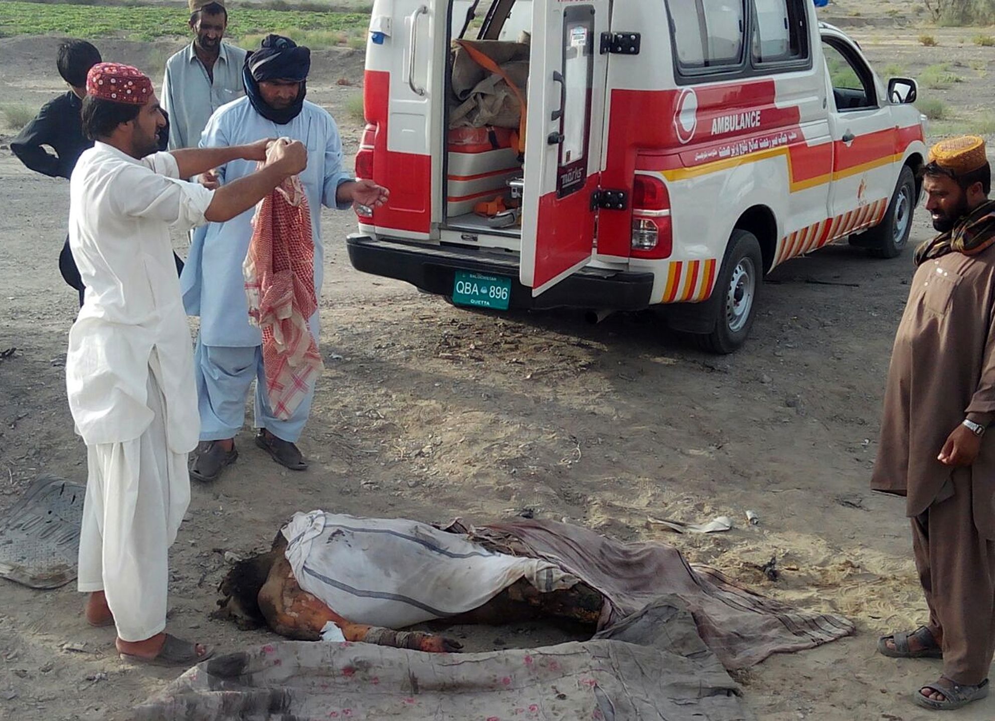 This photo taken by freelance photographer Abdul Malik on Saturday purports to show volunteers standing next to a dead body by the destroyed vehicle in which Mullah Mohammad Akhtar Mansour was allegedly traveling in the Ahmed Wal area in Baluchistan Province of Pakistan, near Afghanistan’s border.
