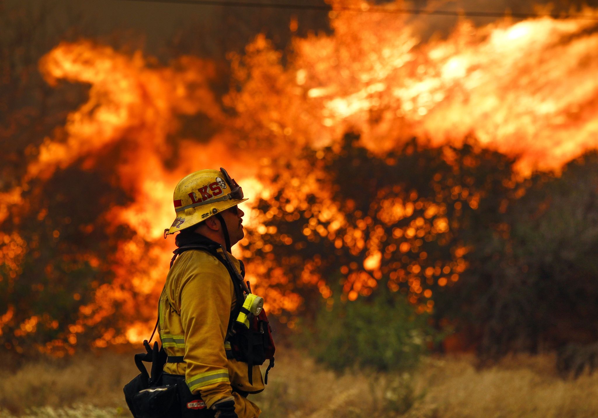 Lakeside firefighter Joe Vasquez watches as large flames burn next to a home on Highway 94 south of Potrero, California, on Monday. An intensifying heat wave stretching from the West Coast to New Mexico threatened to make the fight against Southern California wildfires more difficult Monday.