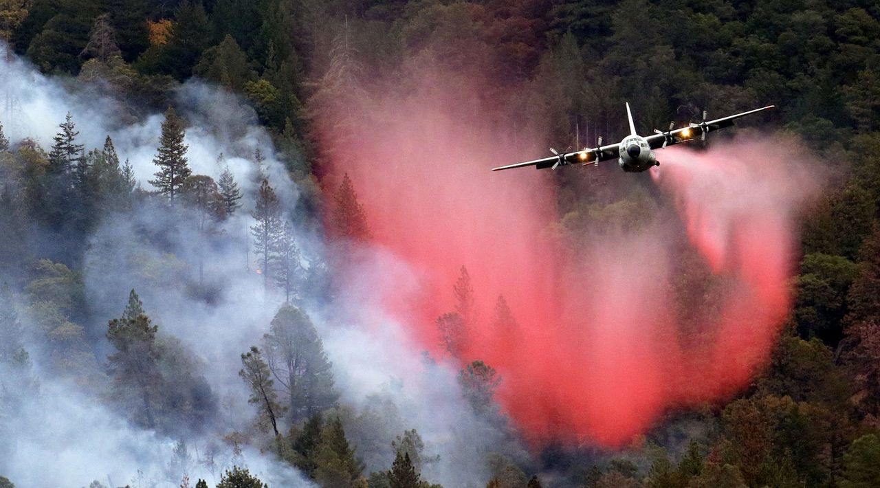 In this Sept. 15, 2015, photo, a firefighting plane drops a load of fire retardant over a smoldering hillside in Middletown, California.