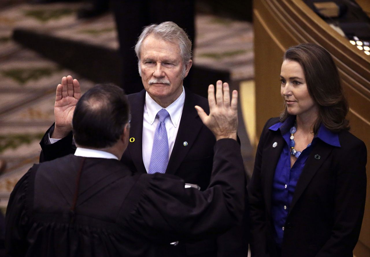In this Jan. 12, 2015, photo, Oregon Gov. John Kitzhaber (center) is joined by his fiancee, Cylvia Hayes, as he is sworn in for an unprecedented fourth term by Senior Judge Paul J. De Muniz in Salem, Oregon.