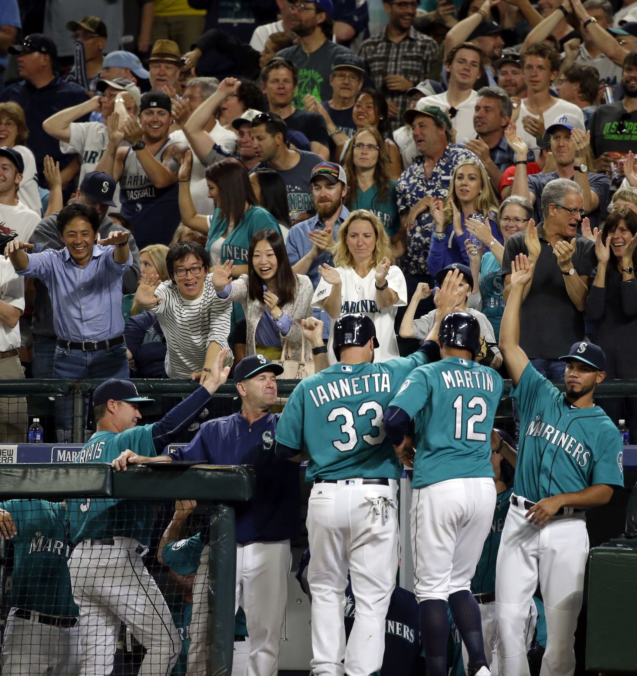 Fans cheer as the Mariners’ Chris Iannetta (33) and Leonys Martin (12) are greeted at the dugout by Luis Sardinas (right) after Iannetta and Martin scored on a three-run triple by Ketel Marte against the Angels on Friday.
