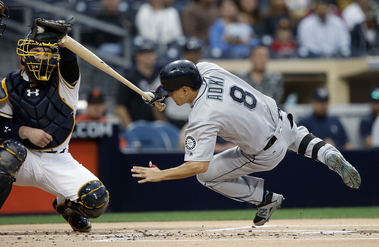 The Mariners’ Norichika Aoki (8) leaps out of the way to avoid a pitch in fron of Padres catcher Derek Norris during the first inning of a game Wednesday in San Diego.