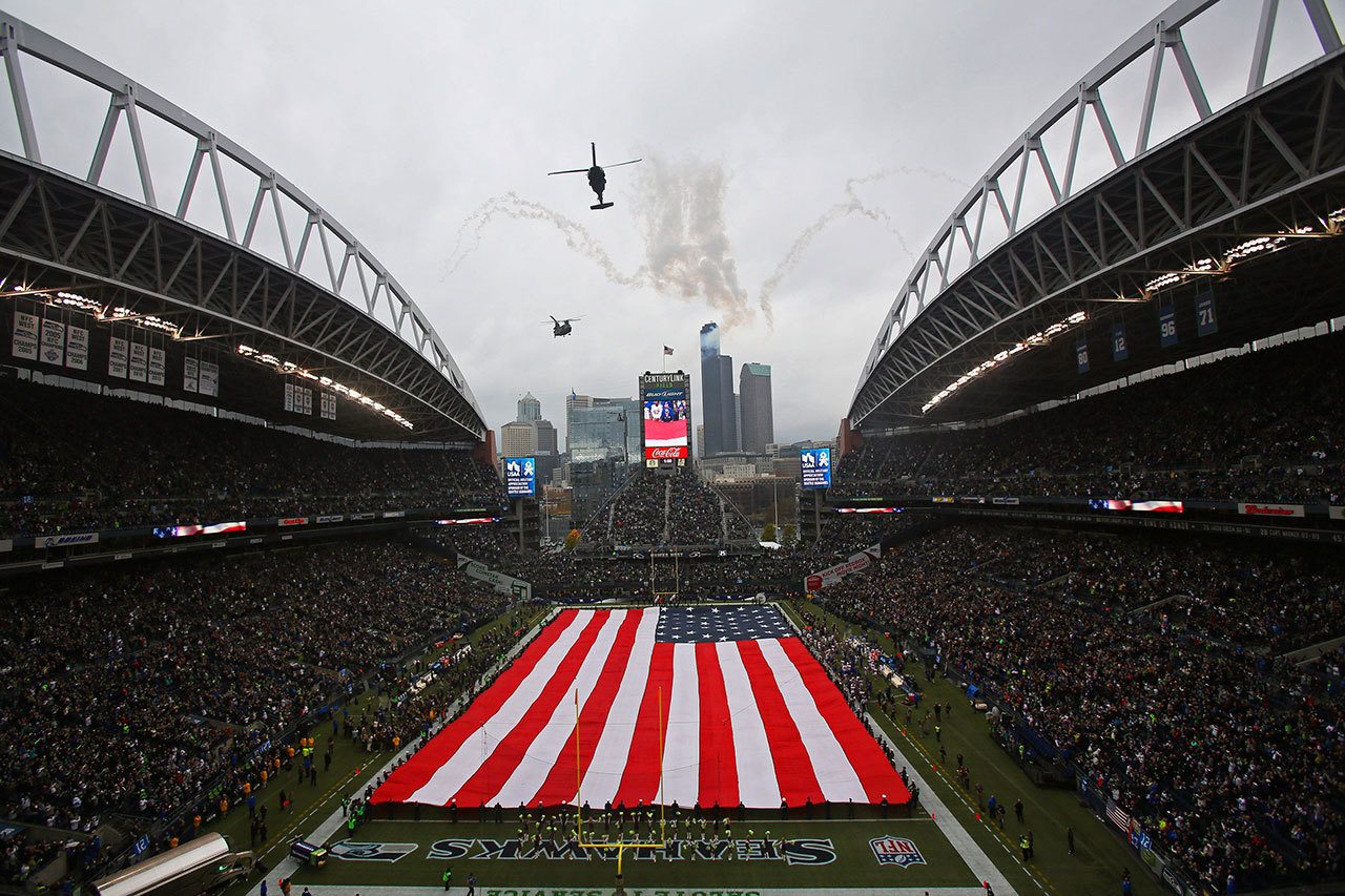 Members of the U.S. Armed Forces unfurled a giant flag over CenturyLink Field as two military helicopters fly over head, before the start of a Seahawks in 2014. (Genna Martin / Herald file photo)
