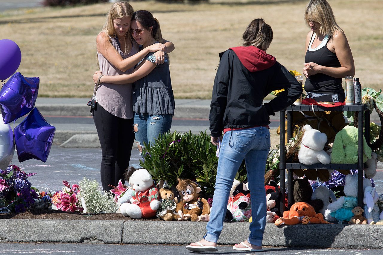Mourners visit a memorial and write chalk notes to the three victims of a Saturday morning shooting, in a parking lot at Kamiak High School on Monday in Everett. (Andy Bronson / The Herald )