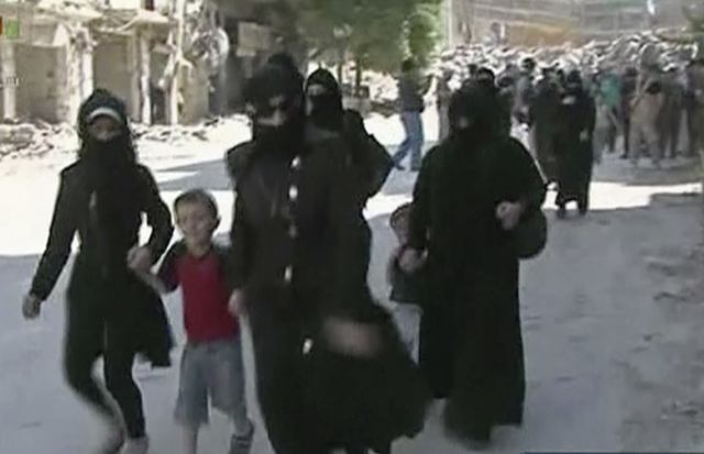 This still image from Syrian state TV video shows women and children arriving in a street lined with heavily damaged buildings in the government-held part of the Salaheddine neighborhood of Aleppo, Syria, on Saturday. The Russian military says 169 civilians have left through the corridors since they were set up, but Syrian opposition activists say no civilians have left besieged parts of the city. (Syrian State TV, via AP)