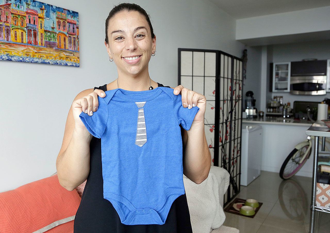 Jessica Ardente holds up a onesie for her unborn baby in her apartment in Miami on Wednesday. (AP Photo/Lynne Sladky)