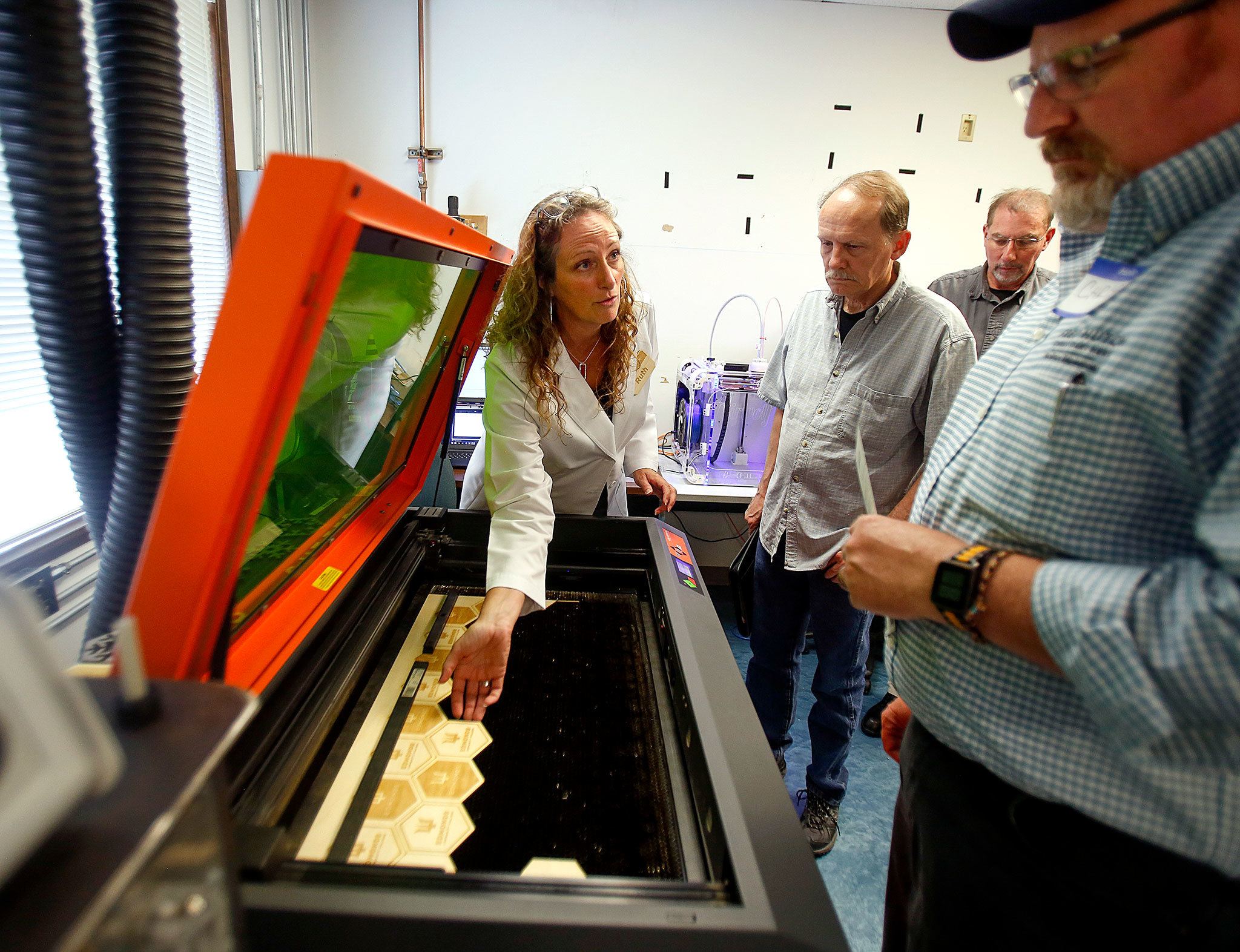 Teacher Ruth Voetmann (left) demonstrates a laser cutter at the grand opening of the new Rapid Proto Lab on Monday at Edmonds Community College. The lab provides demonstrations and answers questions for a large mix of peopleinterested in the new program offering community and student access to special 3D printing, scanning and relatedequipment. (Dan Bates/The Herald)