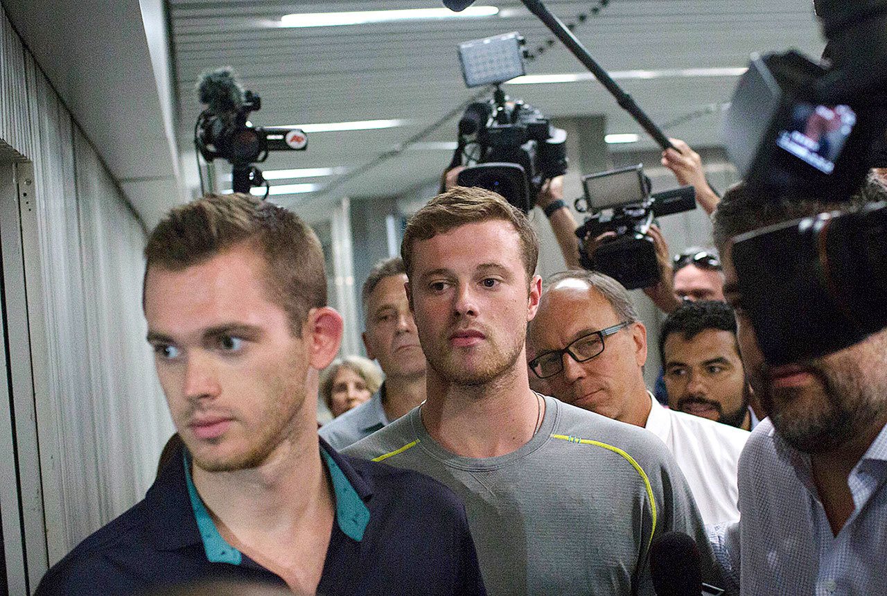 Journalists surround American Olympic swimmers Gunnar Bentz, left, and Jack Conger, center, as they leave the police station at Rio International airport early Thursday. The two were taken off their flight from Brazil to the U.S. on Wednesday by local authorities amid an investigation into a reported robbery targeting Ryan Lochte and his teammates. (AP Photo/Mauro Pimentel)