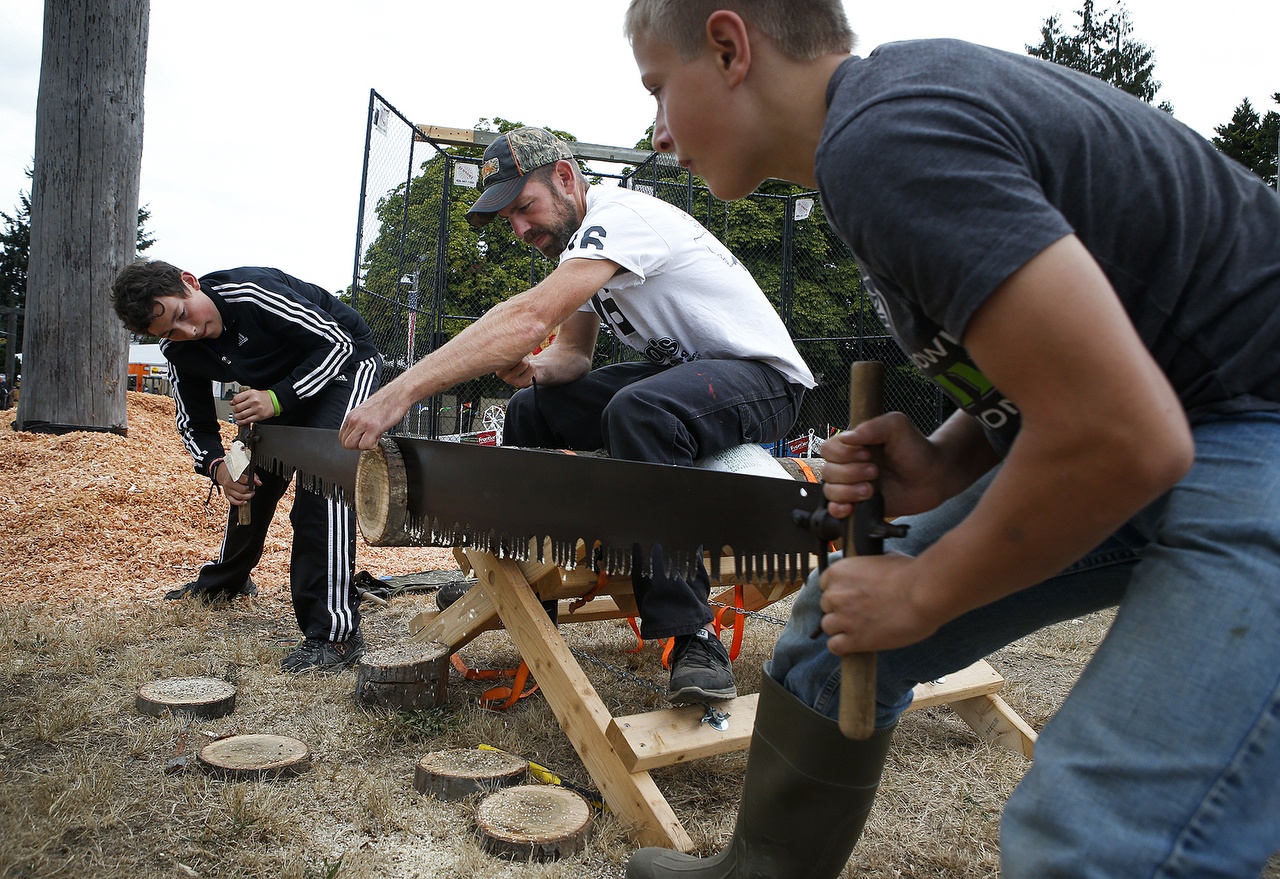 Brandon Becker (left), 13, and Declan Bartelheimer (right), 13, work on their double saw technique with a little help from Eric Hoberg, of Clinton, Montana, during a youth lumberjack competition at the Evergreen State Fair on Tuesday. Seven stations were setup where kids from kindergarten to high school could practice various skills associated with cutting lumber. (Ian Terry / The Herald)