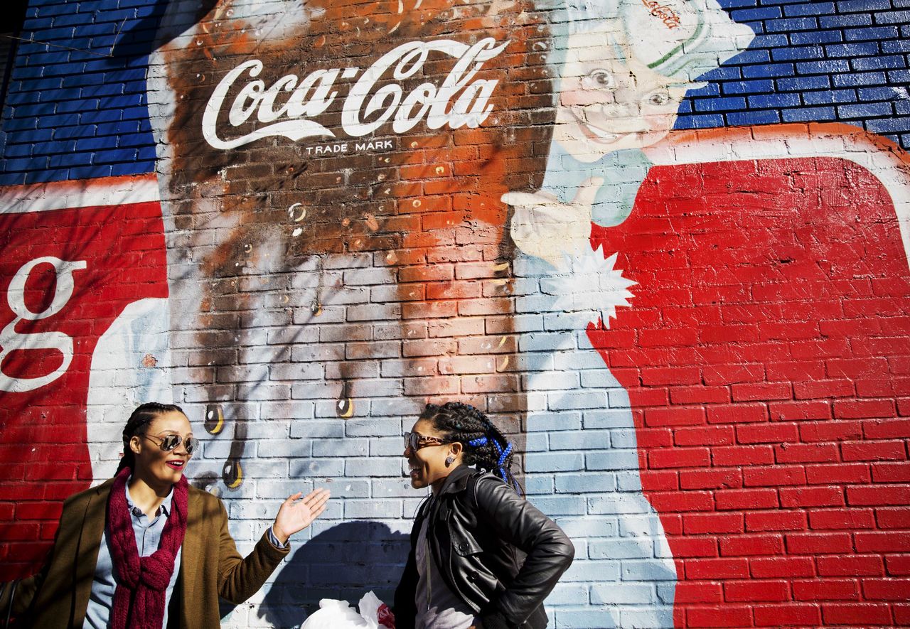Women walk past a mural advertising Coca-Cola on Thursday in Atlanta.