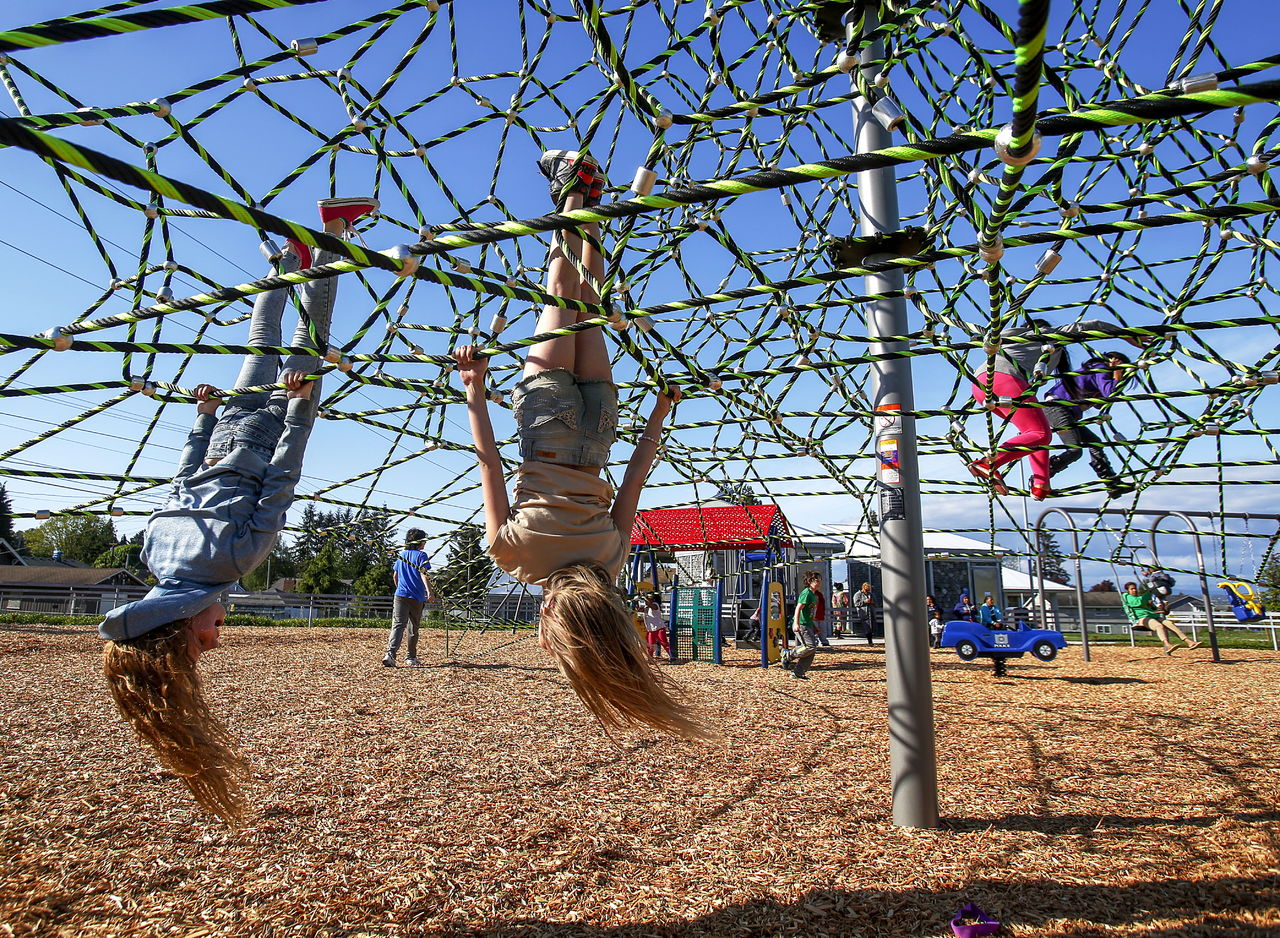 Friends Layla Taylor (left), 11, and Amberle Peterson, 10, hang upside down Monday on a new climbing attraction at the Henry M. Jackson Park in Everett.