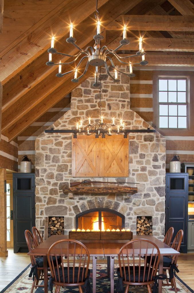 The rustic stone fireplace in this log-and-timber home, designed by Rill Architects, creates a warm and cozy dining experience.
