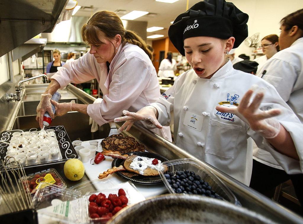 Odyssey Elementary School fifth-grader, Sadie Haworth (right) works on her “reindeer pancakes” with help from mentor, Pam Cox, a cook from the district’s Central Kitchen.

