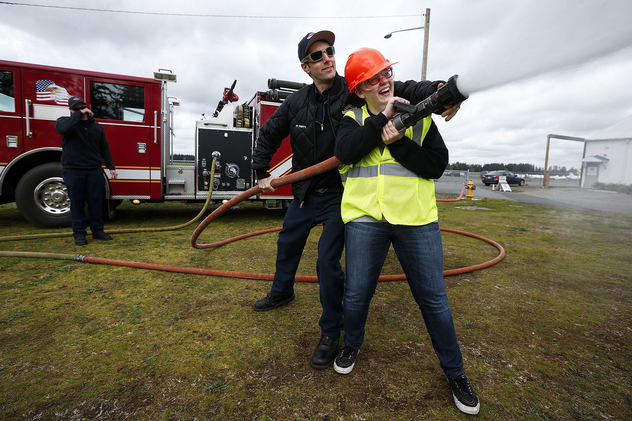 Nicole McGowan, a senior at Arlington High School, gets a helping hand with a fire hose from Ian Phipps of North County EMS on Tuesday during the Snohomish County Trade UP event, which was held on the grounds of Arlington Airport. Organized by Workforce Snohomish and Snohomish County Labor Council, the event, which holds another session April 12 at Sno-Isle Tech Center, gives students from Snohomish County a chance to learn about and gain hands on experience with a variety of trades.