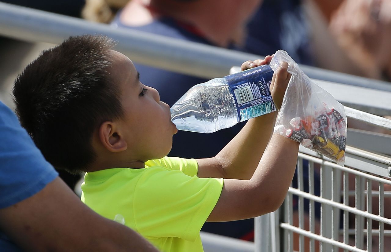 In near record heat, a young baseball fan takes a drink during a Cactus League baseball game between the Cincinnati Reds and the Cleveland Indians on Wednesday in Goodyear, Arizona.