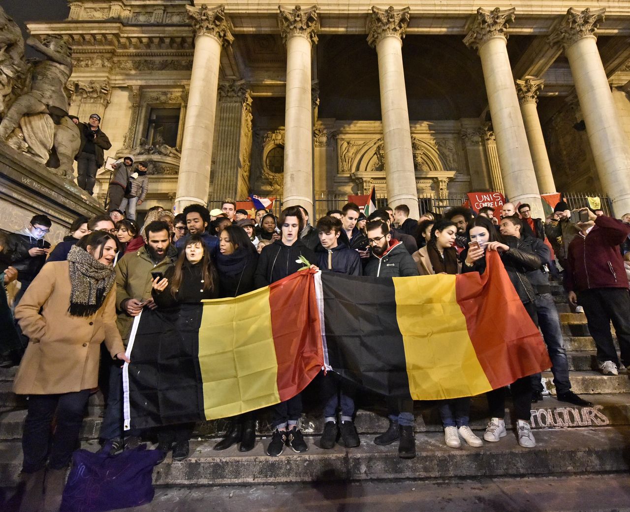 People sing at Place de la Bourse, Brussels, to mourn and demonstrate unity Wednesday evening. Bombs exploded yesterday at the Brussels airport and one of the city’s metro stations, killing and wounding scores of people, as a European capital was again locked down amid heightened security threats.