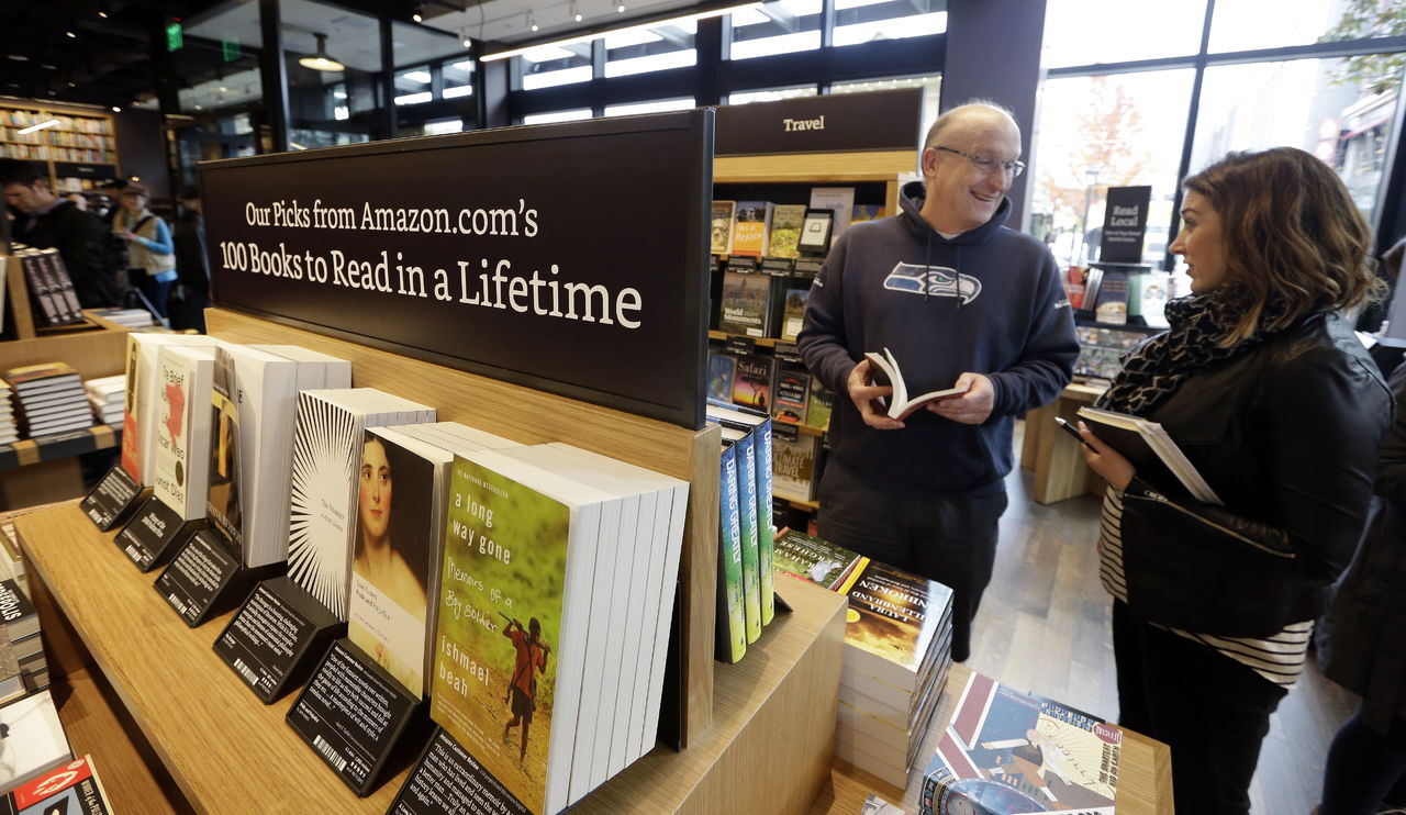 Customer Jeff Edward talks with Amazon employee Sarah Gelman as Edward shops at the opening day for Amazon Books, the first brick-and-mortar retail store for online retail giant Amazon on Nov. 3, 2015, in Seattle. The company said at the time the Seattle store would be a physical extension of its website, combining the benefits of online and traditional book shopping. Prices at the store will be the same as books sold online.