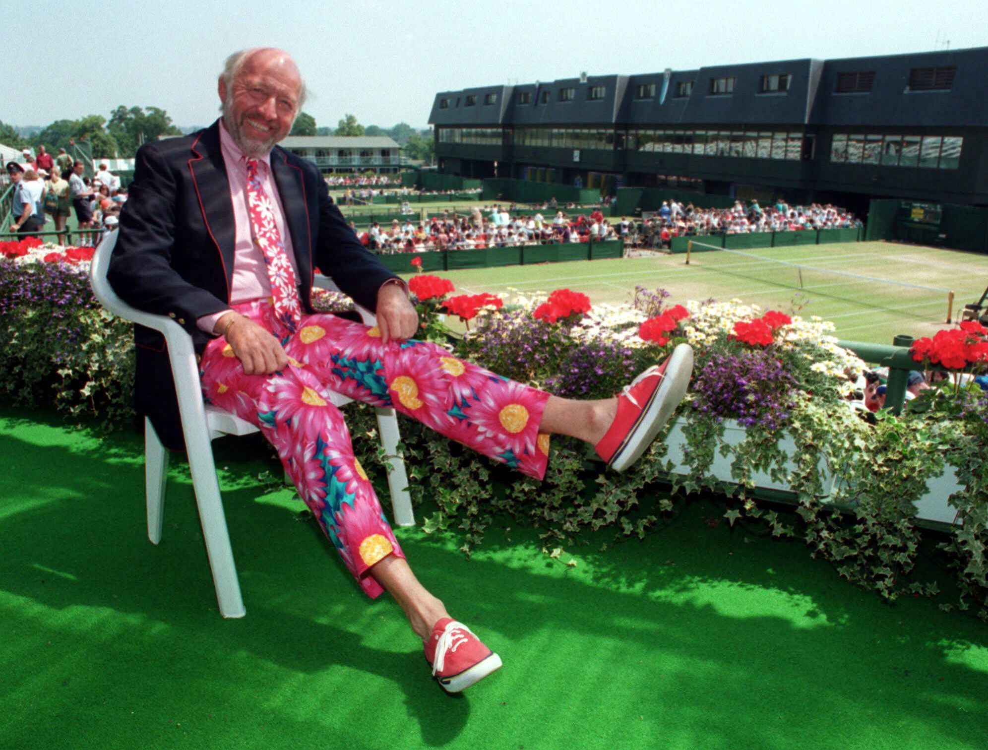 In this June 30, 1993, NBC tennis commentator Bud Collins displays a pair of brightly colored trousers as he sits overlooking the courts at Wimbledon, England. Collins, the tennis historian and American voice of the sport in print and on TV for decades, died Friday at his home in Brookline, Mass.