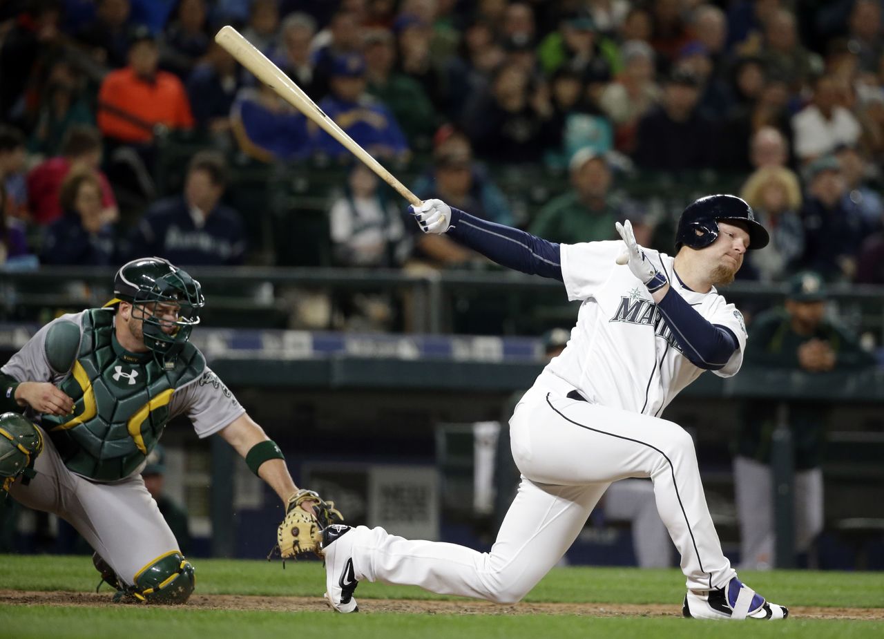 The Mariners’ Adam Lind swings and misses as he strikes out to end the game in front of Athletics catcher Stephen Vogt on Friday in Seattle.