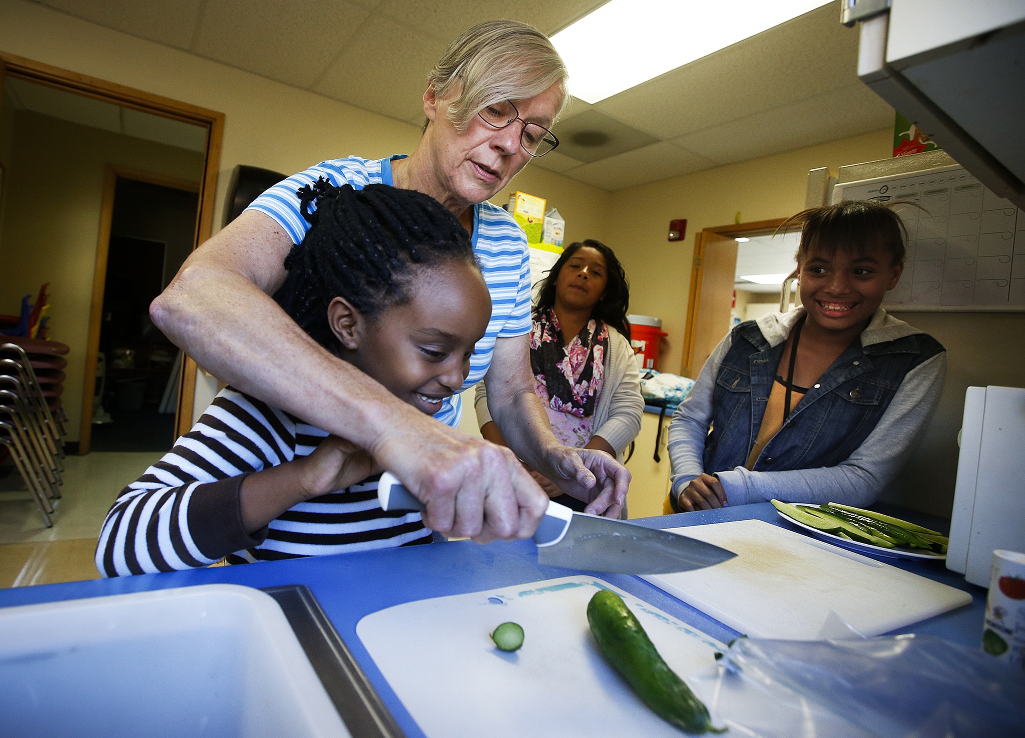 Pat Benefiel, of Lake Stevens, shows Lisa Sheja, 6, how to properly hold a knife before slicing into a cucumber as Ashley Silva-Schmidt (center) and Olivia Evans (right) look on at the East Casino Road YMCA in Everett on Tuesday, Sept. 20. “At first they wouldn’t eat any vegetables, but pretty soon we were mixing them into every meal and they loved it,” Benefiel said, who brings fresh vegetables from her own garden to teach kids in the south Everett area how to cook healthy meals from scratch. (Ian Terry / The Herald)