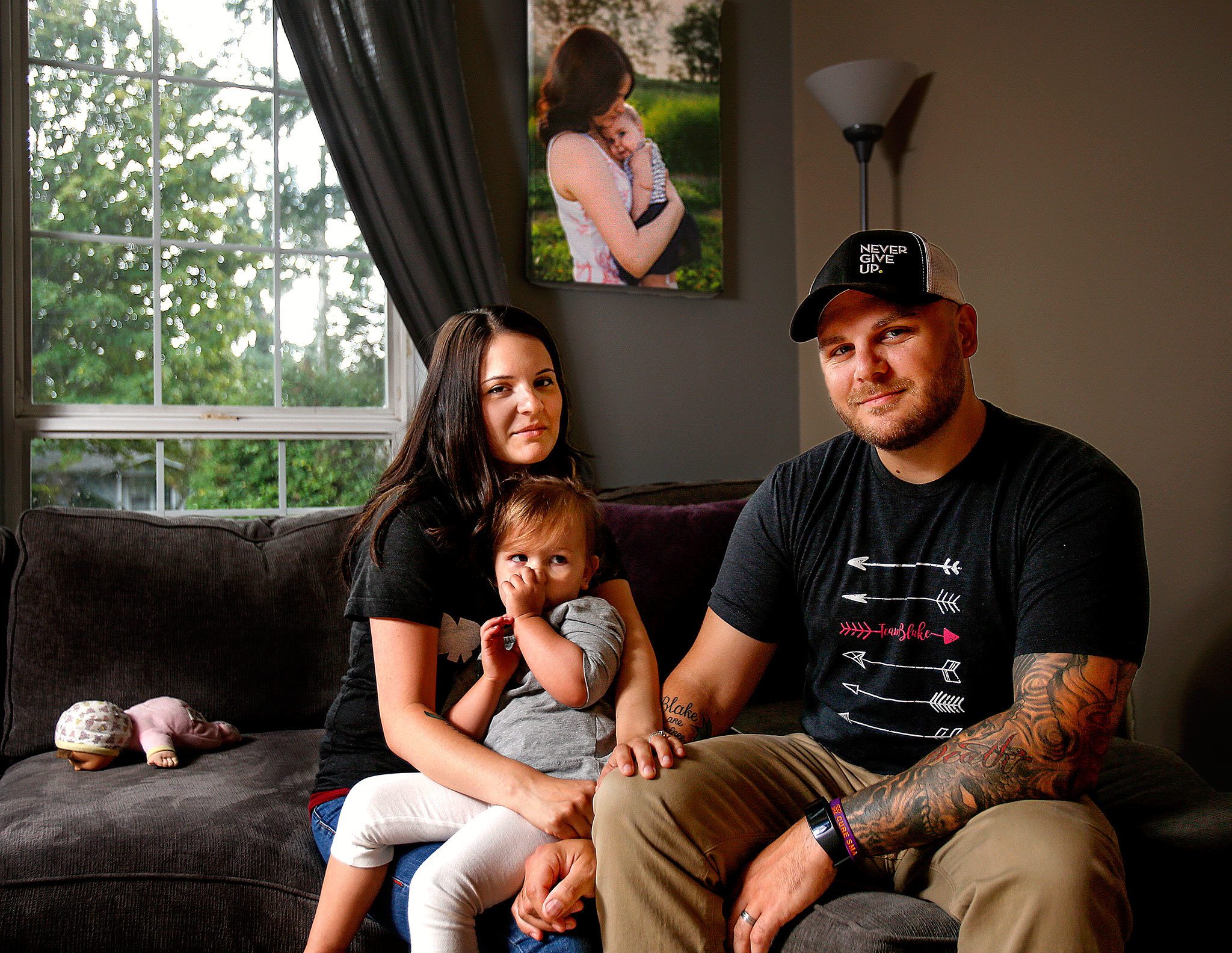 Stephanie and Jeff Reid spend time at home in Marysville with their 2-year-old daughter, Kenley. In a photograph on the wall behind them, Stephanie holds their baby daughter, Blake, who died Aug. 10 of spinal muscular atrophy, or SMA. (Dan Bates / The Herald)
