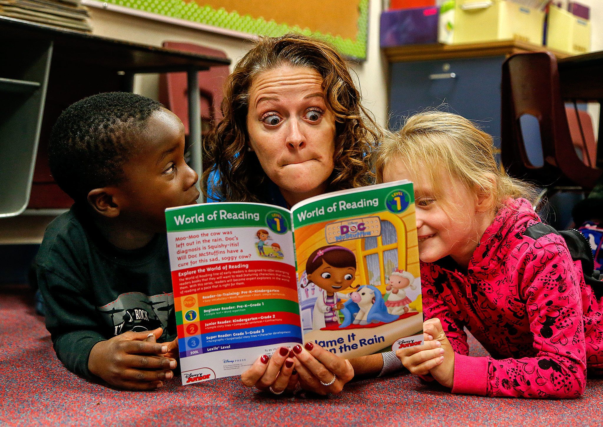 Hawthorne Elementary School kindergarten students Jonas Rugabano (left) and Rileyann Brown are treated Friday to a delightful reading experience while lying on their classroom floor with Day of Caring volunteer Alisha Sylvester. Sylvester, who works at Boeing in 787 quality investigation, said she is a mom, so she’s had some experience with this before. (Dan Bates / The Herald)