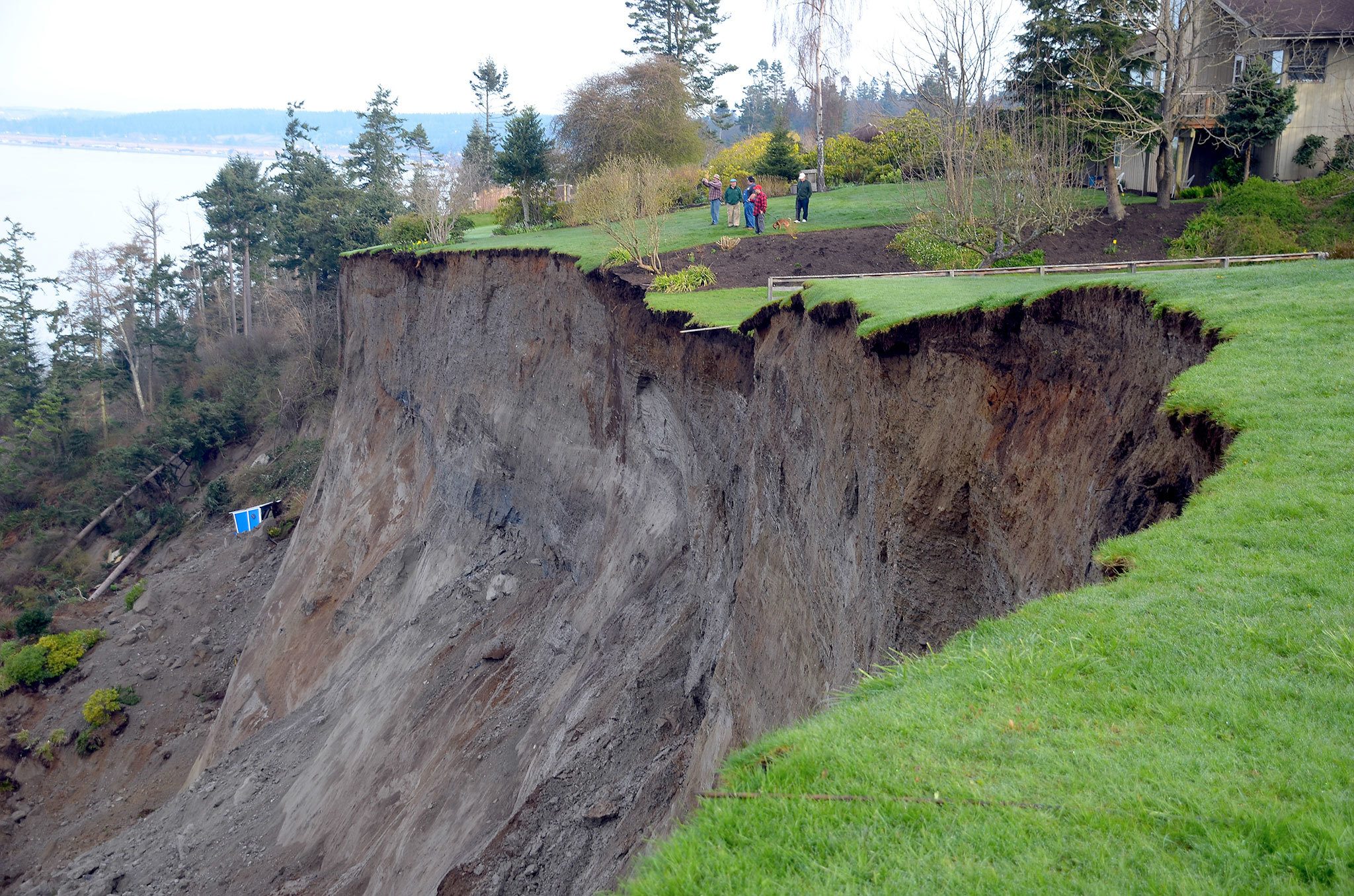 People stand in a yard near a landslide that happened about 4 a.m. on March 27, 2013. An estimated 5.3 million cubic feet of earth, a house and a small wooded area were displaced in a matter of moments, according to a Department of Natural Resources report. The slide destroyed part of Driftwood Way and damaged many properties. Nobody was injured. (Photo Courtesy The Whidbey News-Times)
