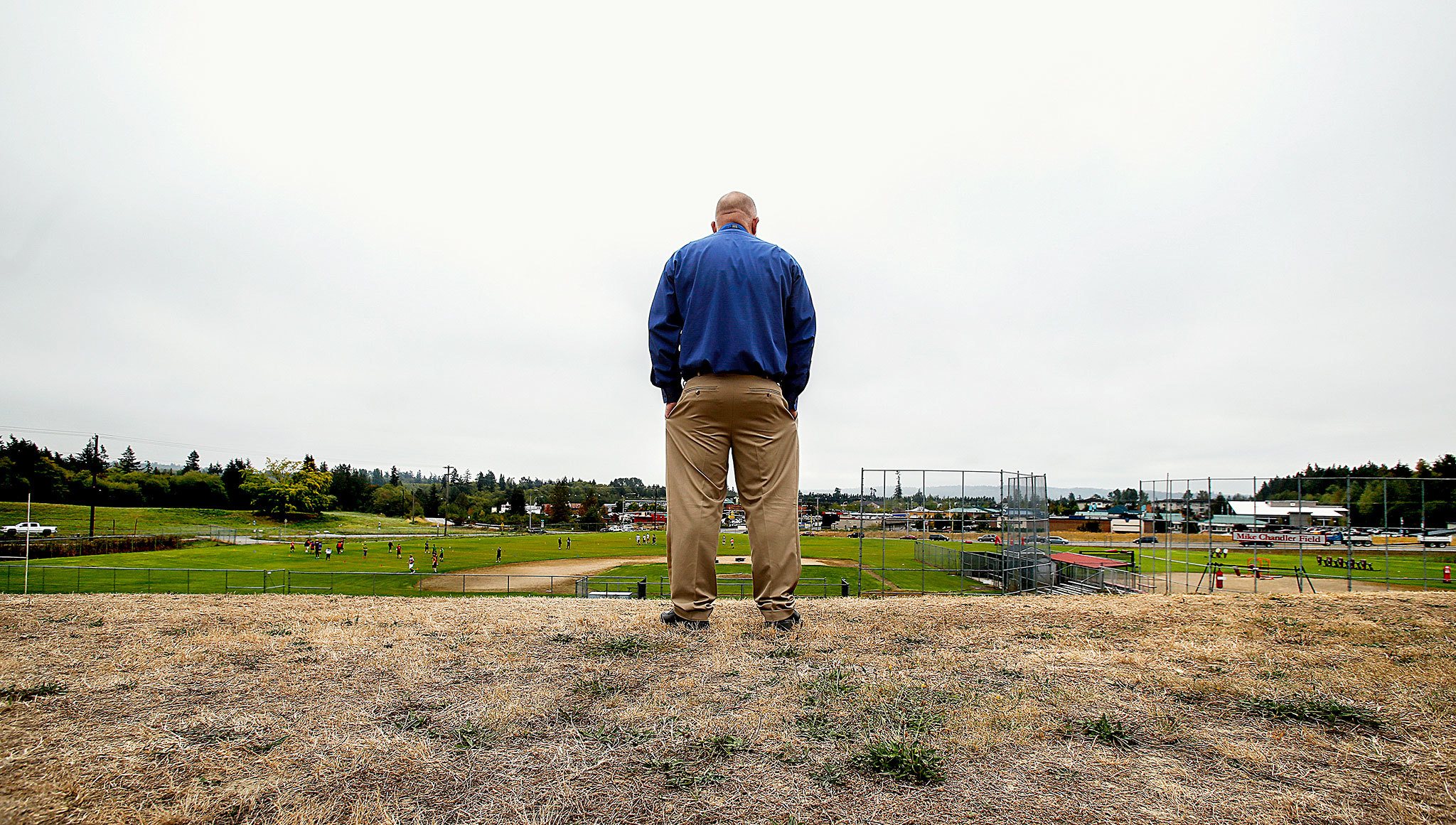 Dean of Students Ross Short watches several large groups of students performing and playing on the massive fields on the south side of Stanwood High School’s 63-acre campus. He said they would like to build the new school into the base of the hillside that rises just beyond where he is standing. (Dan Bates/ The Herald)