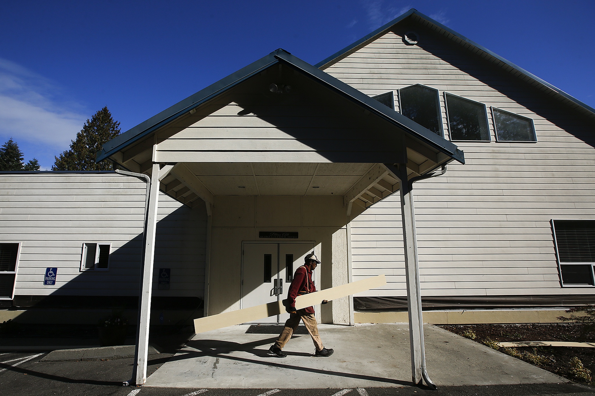 Otis Campbell, of Stanwood, a member of The Seven Lakes Baptist Church, carries a board while helping to replace the siding on his church on Sept. 10. Members of the Lakewood ward of the Church of Jesus Christ of Latter-day Saints volunteered to help The Seven Lakes Baptist Church with repairs. (Ian Terry / The Herald)